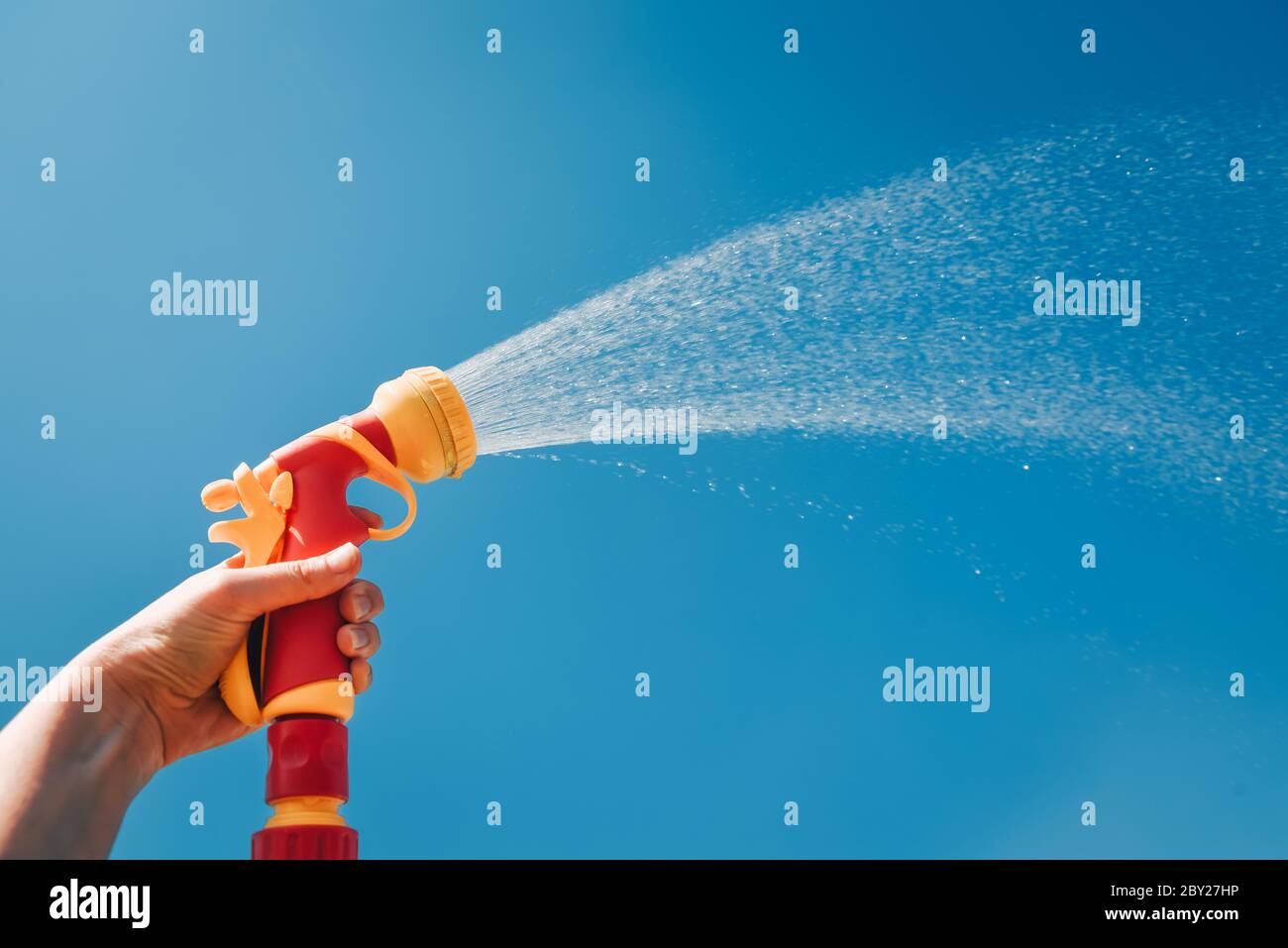 Hand hält gelben Schlauch mit Düse auf Hintergrund des blauen Himmels mit Wasserspritzern Stockfoto