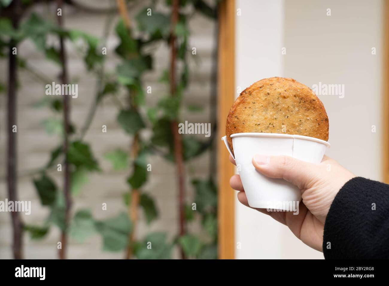 Hand hält einen koreanischen traditionellen frittierten Pfannkuchen, Hotteok, mit süßen Füllungen in einer Tasse. Beliebte koreanische Street Food. Stockfoto