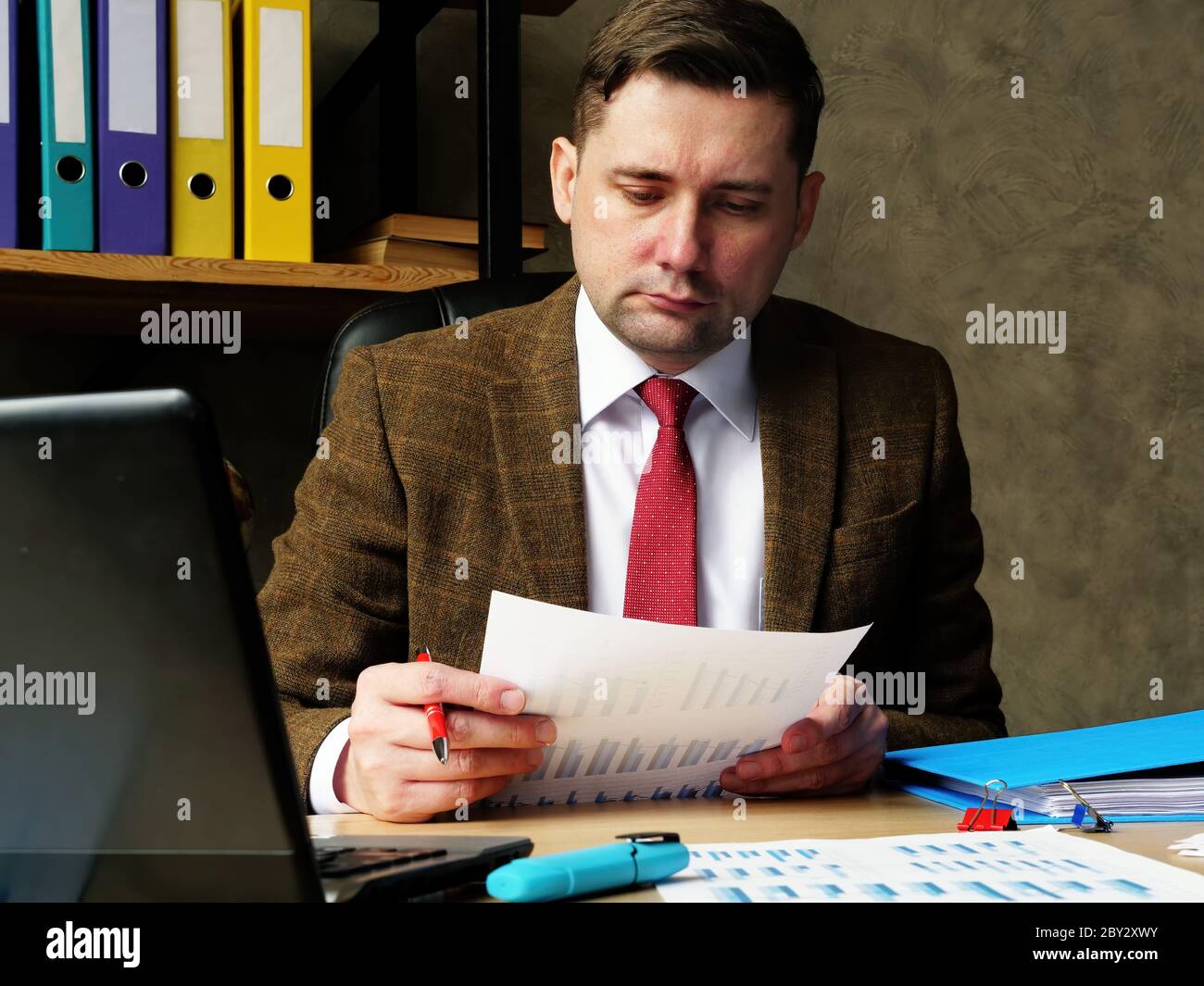 Ein Mann in einem Anzug arbeitet mit Papieren und prüft Daten mit Diagrammen. Büroarbeiten. Stockfoto