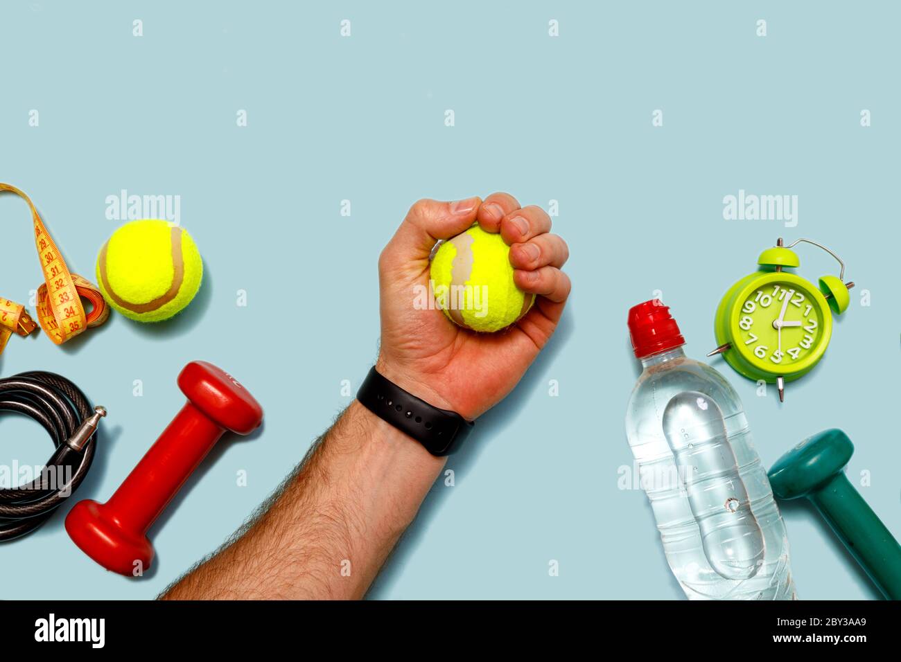 Flach liegend schießen von grünem Wecker, Tennisball, Flasche Wasser,  Maßband, männliche Hand und Hanteln auf pastellblauem Hintergrund.  Draufsicht mit Cop Stockfotografie - Alamy
