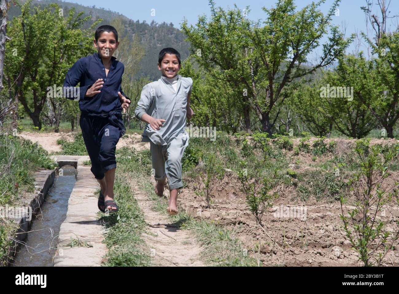Landwirt, der auf einem Feld in Swat Valley, Pakistan, arbeitet. Kinder, die entlang der Wasserstraße laufen. Stockfoto