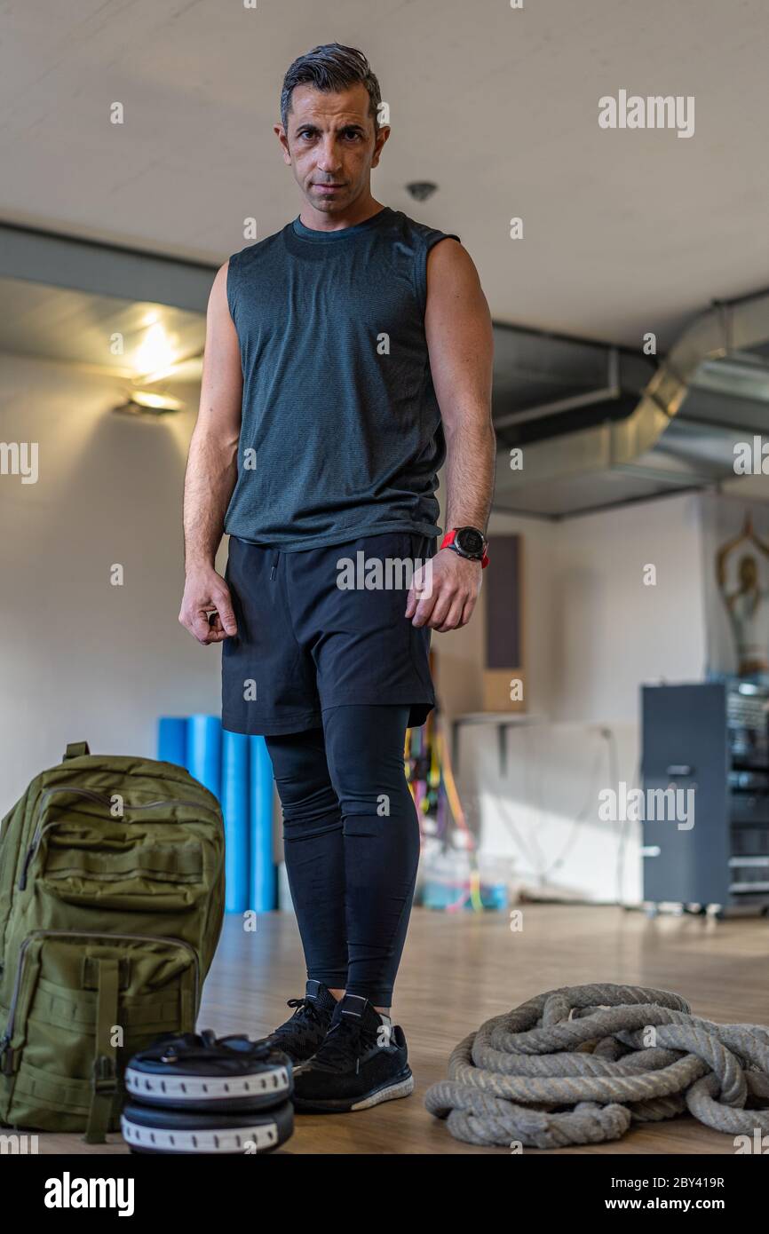 Motivierter Bootcamps-Trainer steht mit Fitnessgeräten in der Turnhalle. Hanteln, Wasserkocher, Seil, Sandsack auf Holzboden. Porträt des libanesischen inst Stockfoto