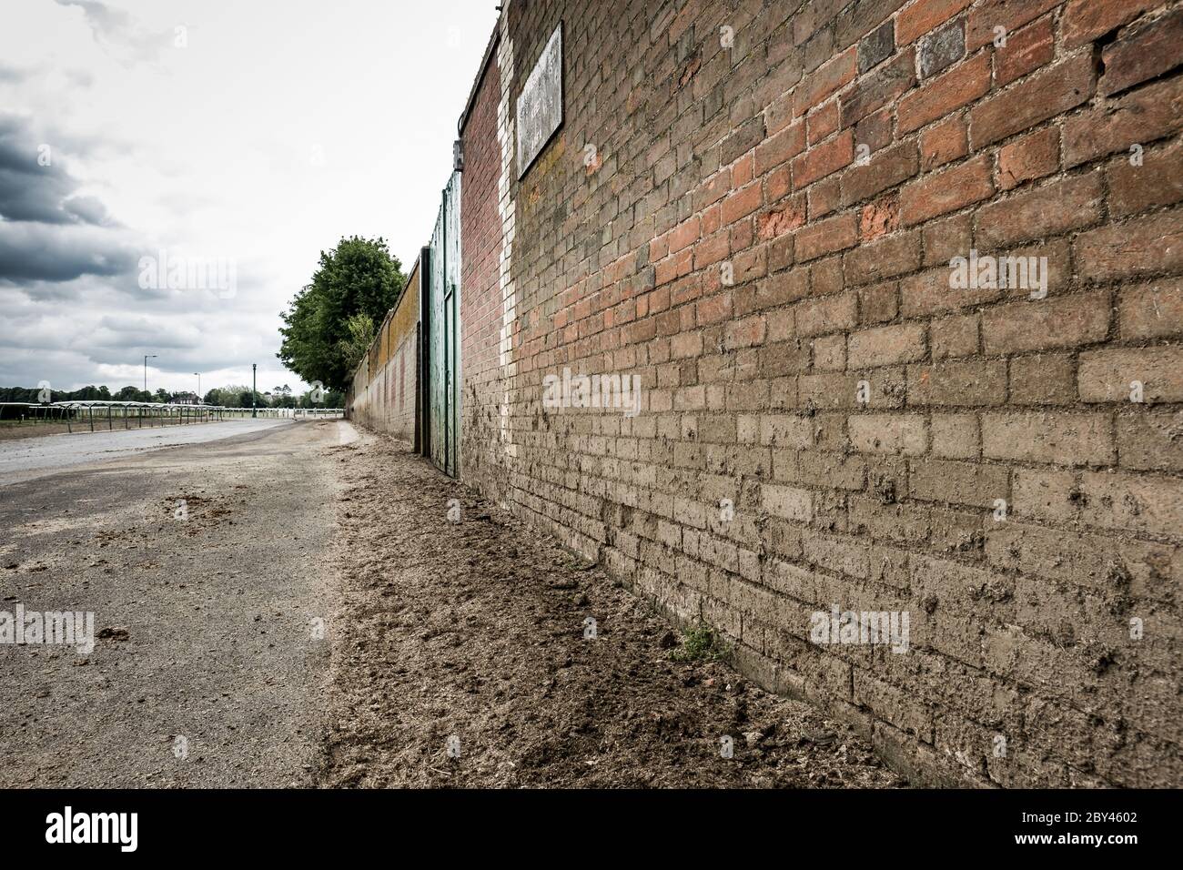 Raue strukturierte Oberfläche einer verwitterten Ziegelwand, die den getrockneten Schlamm auf der unteren Hälfte der Wand und der angrenzenden Straße zeigt. Stockfoto