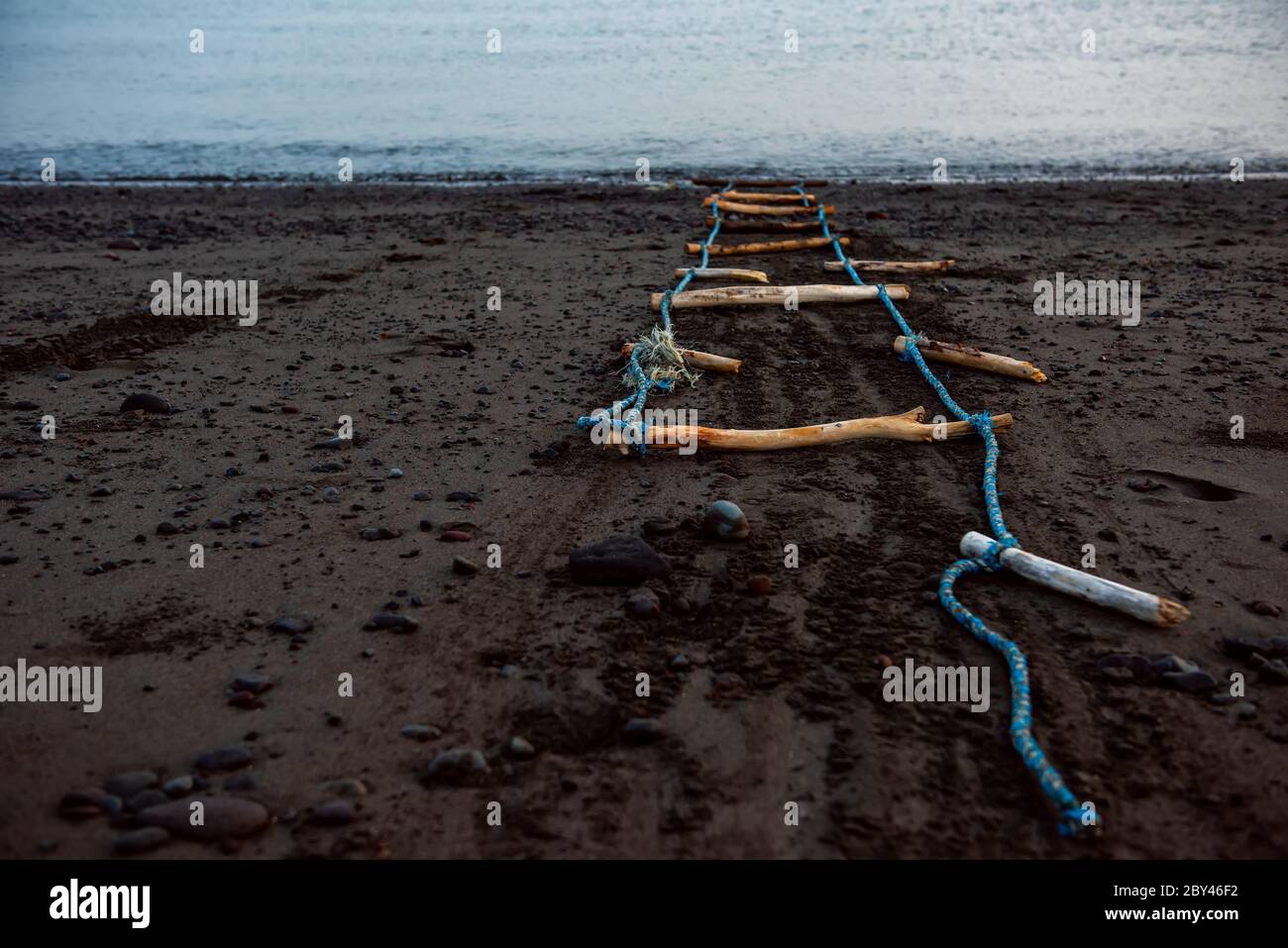 Treppen ins nichts. Handgemachte alte Holztreppe am schwarzen Sandstrand. Bali, Indonesien Stockfoto