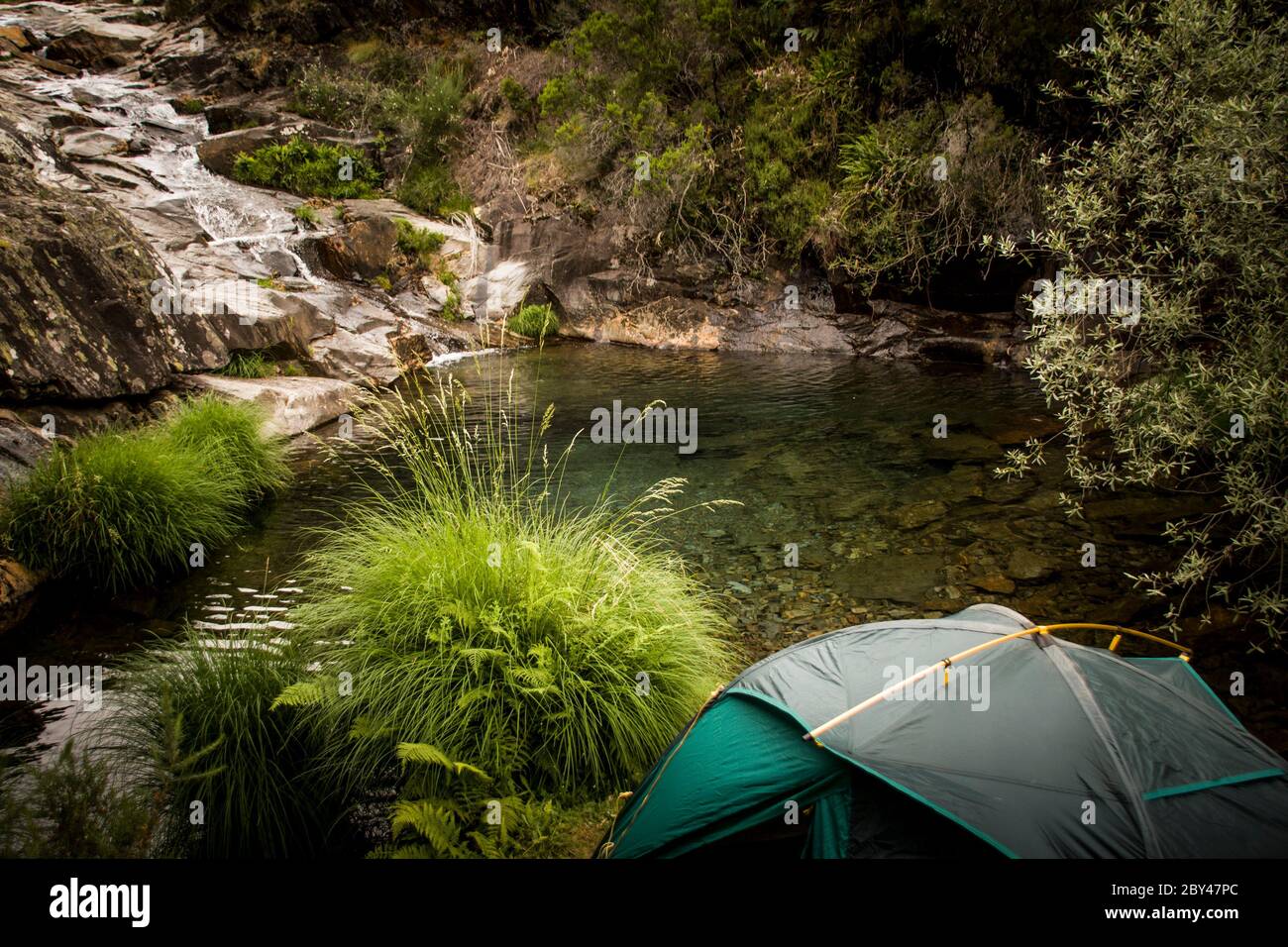 Ein Zelt steht Lager an einem Ufer eines kleinen Sees und Wasserfall für ein wildes Camping, weg von allem. Stockfoto