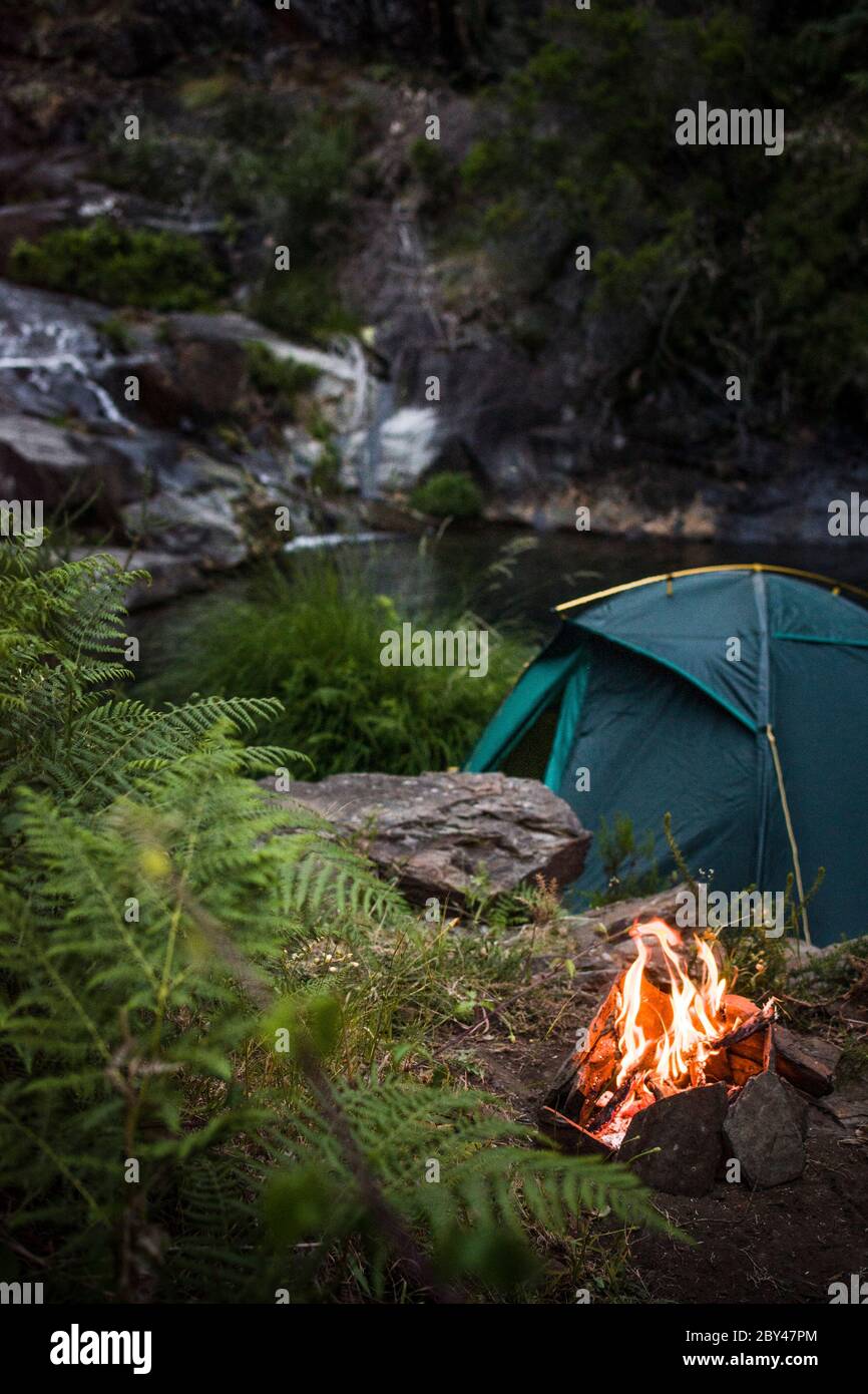 Ein Zelt wild camping in der Nähe eines kleinen Sees und Wasserfall, mit einem kleinen Lagerfeuer brennt auf der Seite. Stockfoto