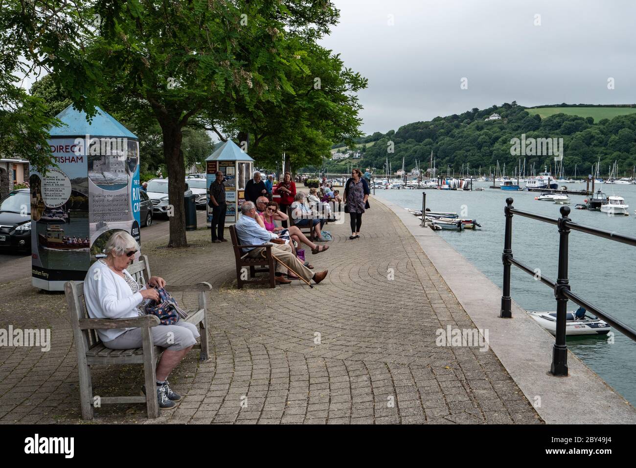 Touristen entspannen auf Sitzbänken am Ufer des Flusses Dart in Dartmouth Devon England. Stockfoto