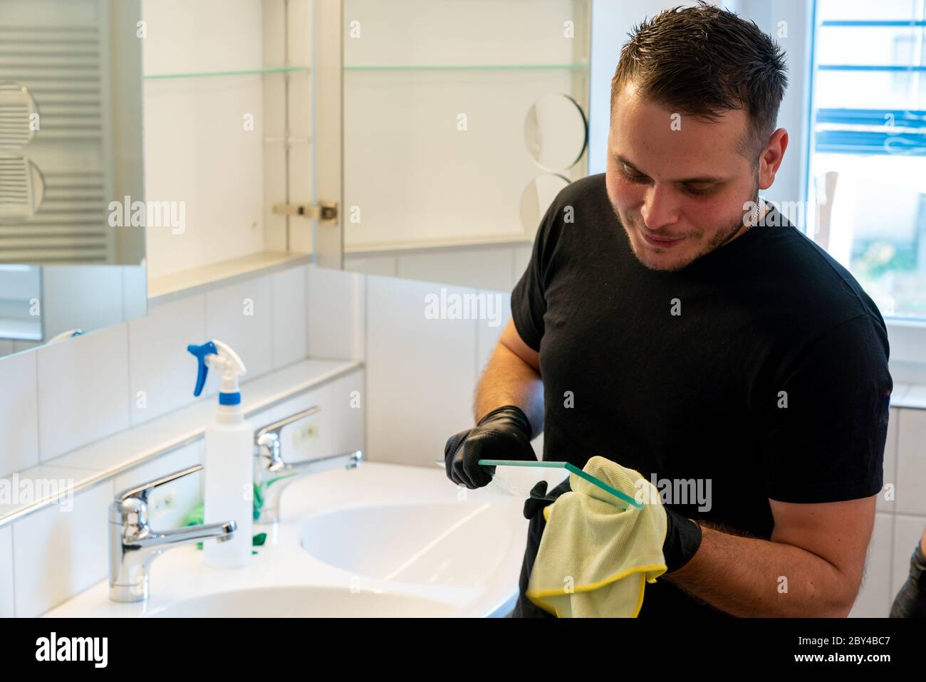 Ein professonaler Reiniger reinigt ein Bad und die Glasablagen im Badschrank Stockfoto