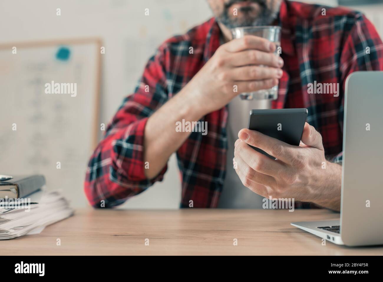 Gig Arbeiter Trinkwasser und mit Handy im Home Office während der freiberuflichen Projektarbeit Stockfoto