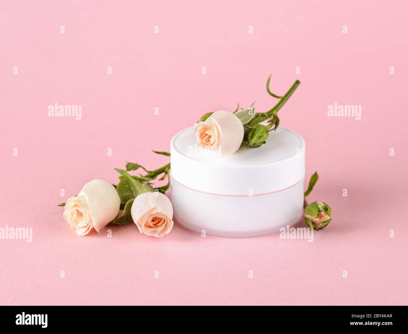 Gesichtscreme und kleine Rosen in hellem Pfirsich-Farbe auf einem pastellrosa Hintergrund. Kosmetik für feuchtigkeitsspendende und reinigende. Haut-, Haar- oder Körperpflege. Stockfoto