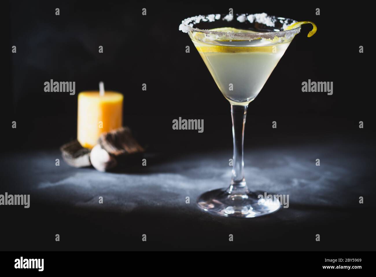 Ein Glas martini auf dunklem Hintergrund mit Zitronenschale und Salz. Duftkerze und Sticks im Hintergrund schaffen Atmosphäre. Stockfoto