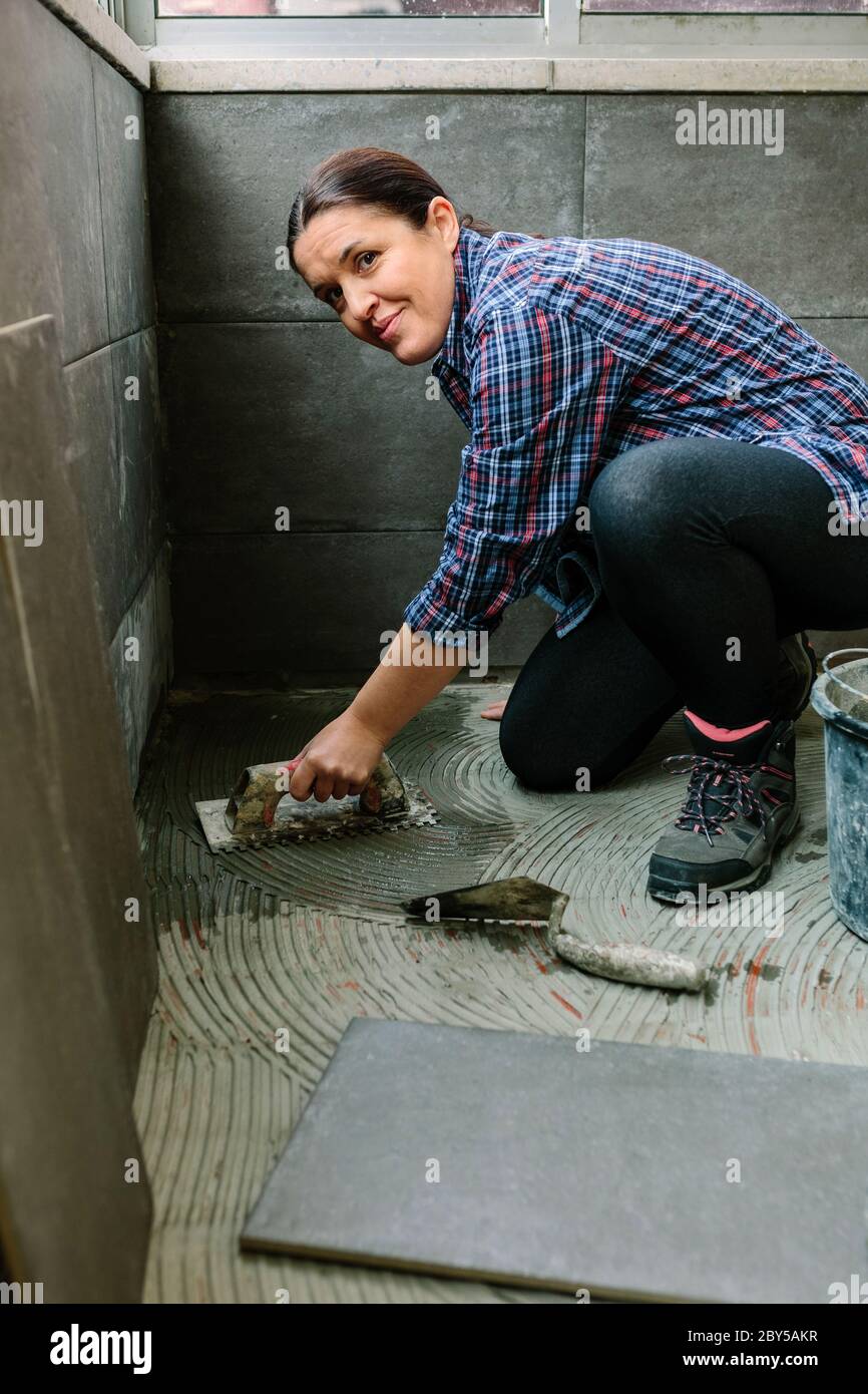 Maurerin legt einen neuen Fliesenboden Stockfoto
