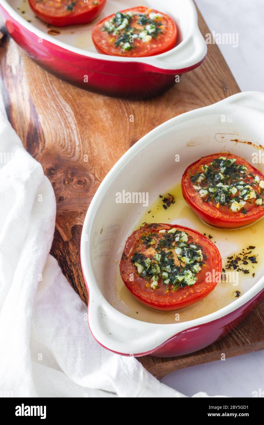 Halbe Tomaten mit Olivenöl, Knoblauch und Petersilie in kleinen roten Ofengerichten gebraten Stockfoto