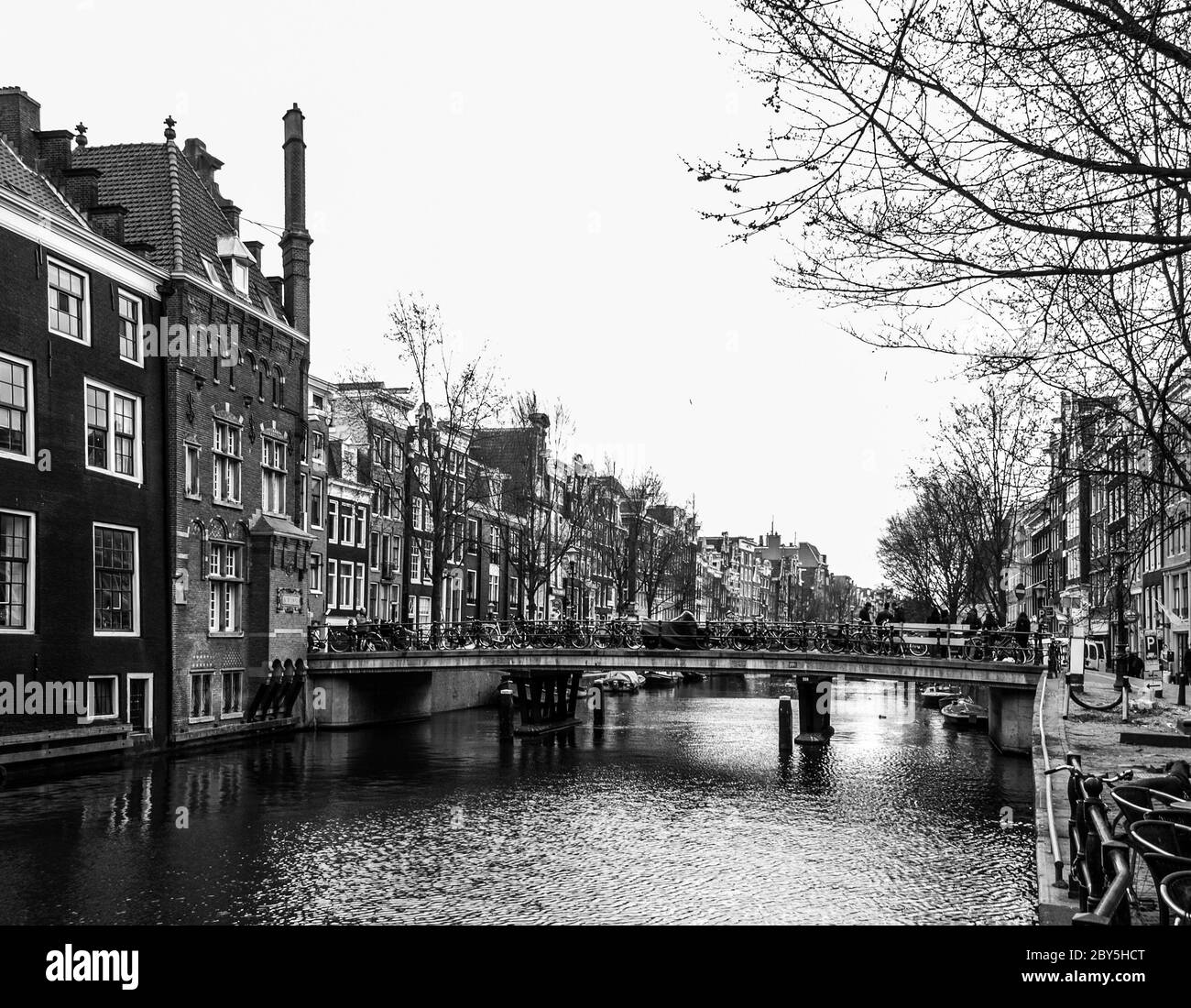 Wasserkanal, auch Gracht genannt, und enge Häuser entlang des Kanals im Zentrum von Amsterdam, Niederlande, schwarz-weiß Bild. Stockfoto