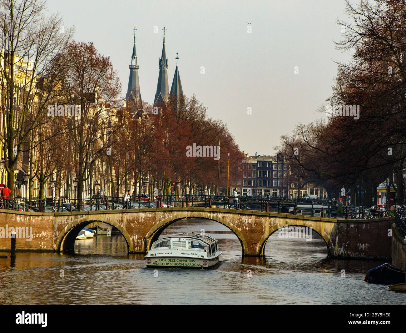 Gracht oder Canal of Amsterdam mit typischer niedriger Brücke und Sightseeing-Boot im frühen Frühling, Niederlande Stockfoto