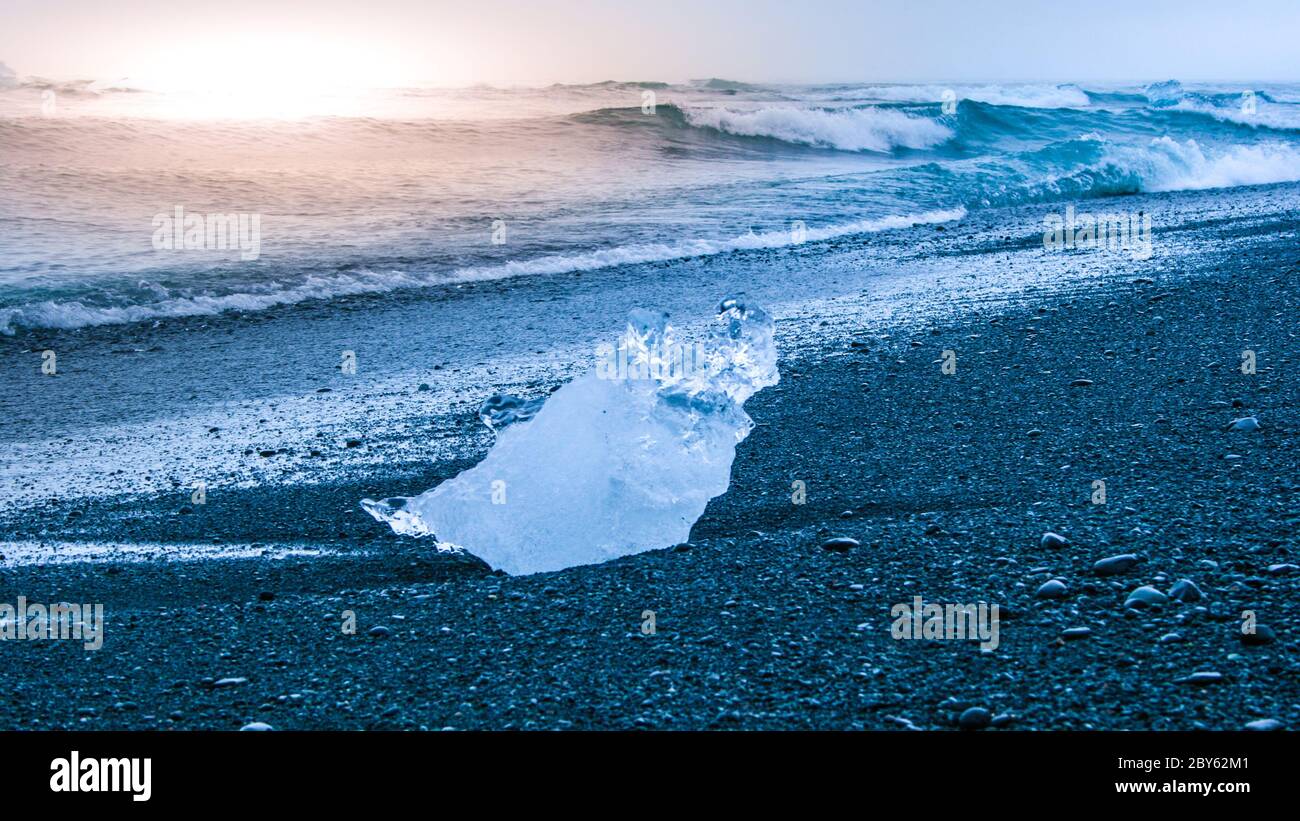 Eisberge, die bei Sonnenaufgang am schwarzen Strand in der Nähe des Jokulsarlon Gletschersees, Island, von Meereswellen überspült werden. Stockfoto