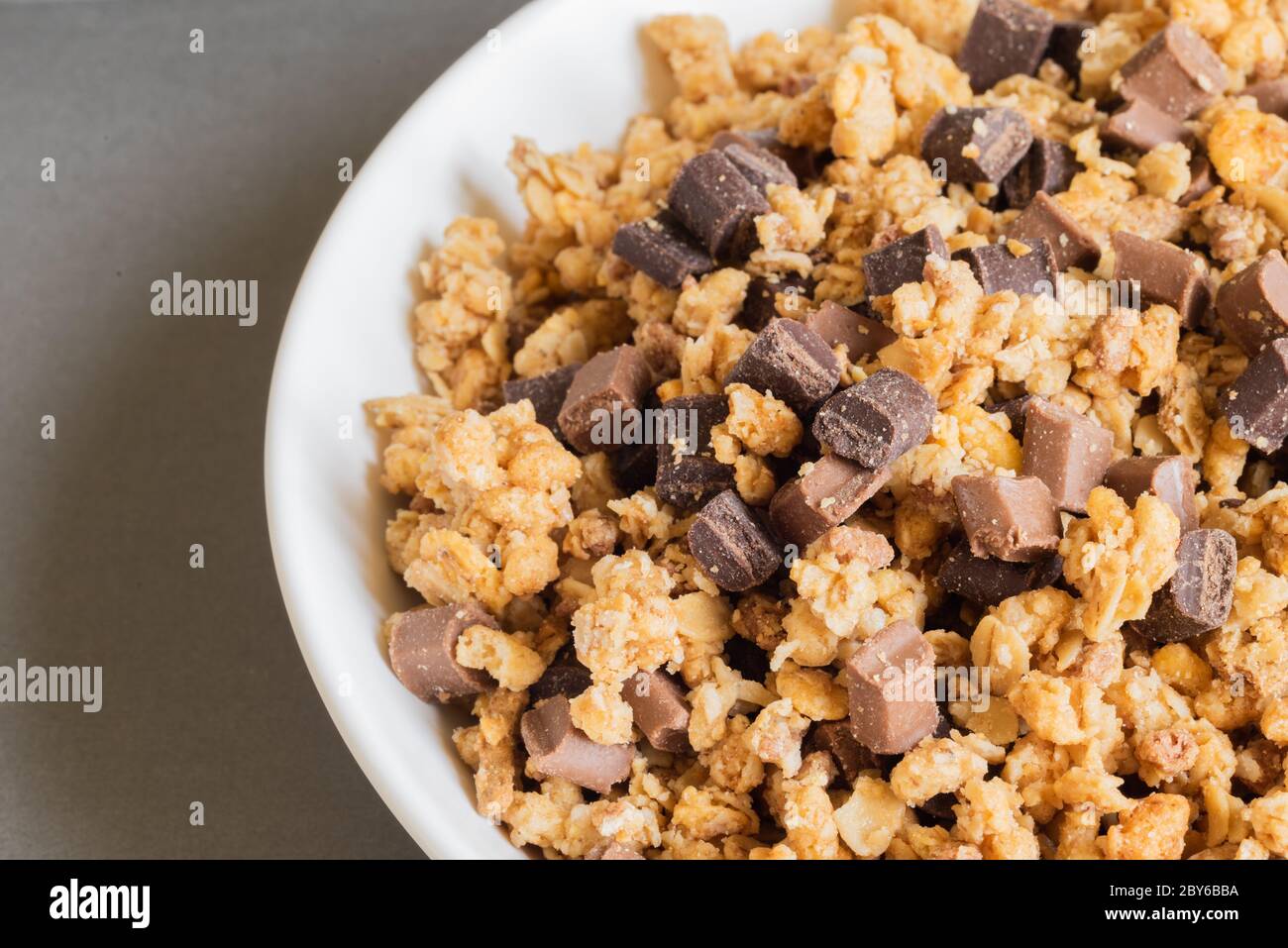 Müsli knusprig muesly mit Stücken von dunkler und Milchschokolade in einer Schüssel auf hellbraunem Hintergrund. Müsli mit Rückendeckung. Draufsicht. Makro. Speicherplatz kopieren. Stockfoto