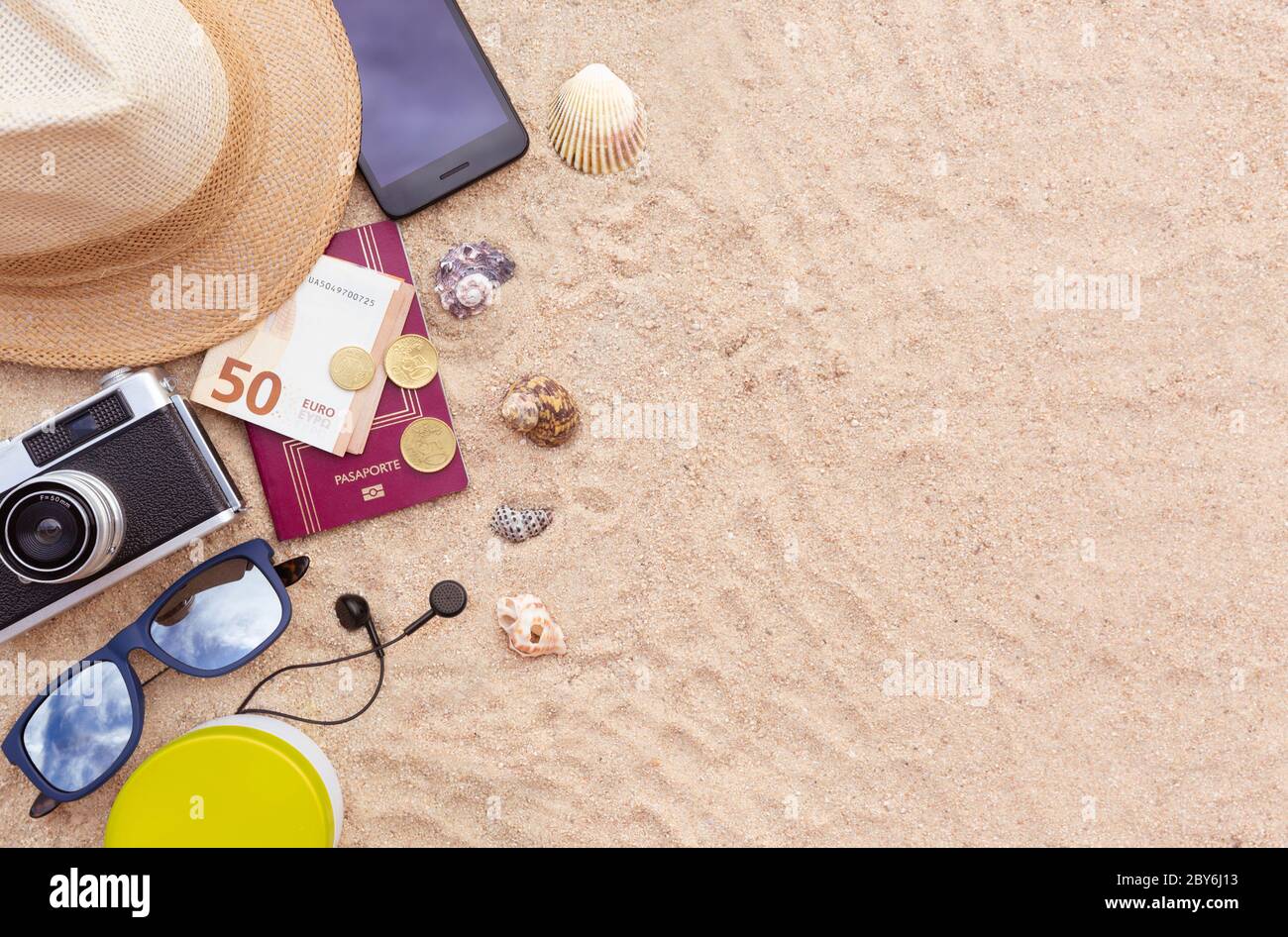 Einige Strandartikel, ein Reisepass und etwas Bargeld, ein Smartphone, Hut, Kamera und Sonnenbrille auf dem Sand. Leerzeichen für Text. Urlaub, Sommer und Strand Konzept. Stockfoto