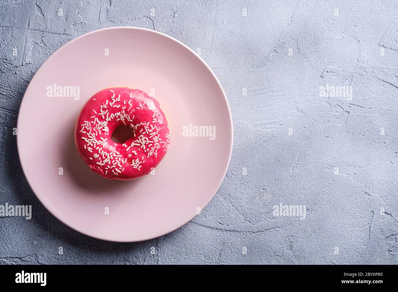 Rosa Donut mit Streuseln auf rosa Teller, süß glasierte Dessert Lebensmittel auf Beton strukturierten Hintergrund, Draufsicht Copy Space Stockfoto