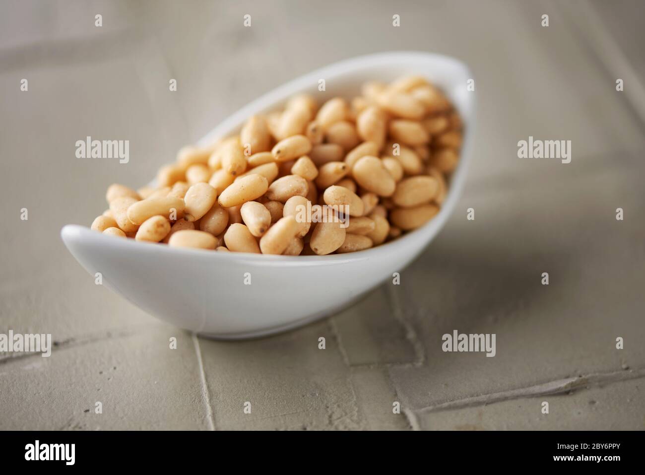 Eine weiße Keramikschale voller geschälter Pinienkerne auf einer strukturierten Betonoberfläche Stockfoto