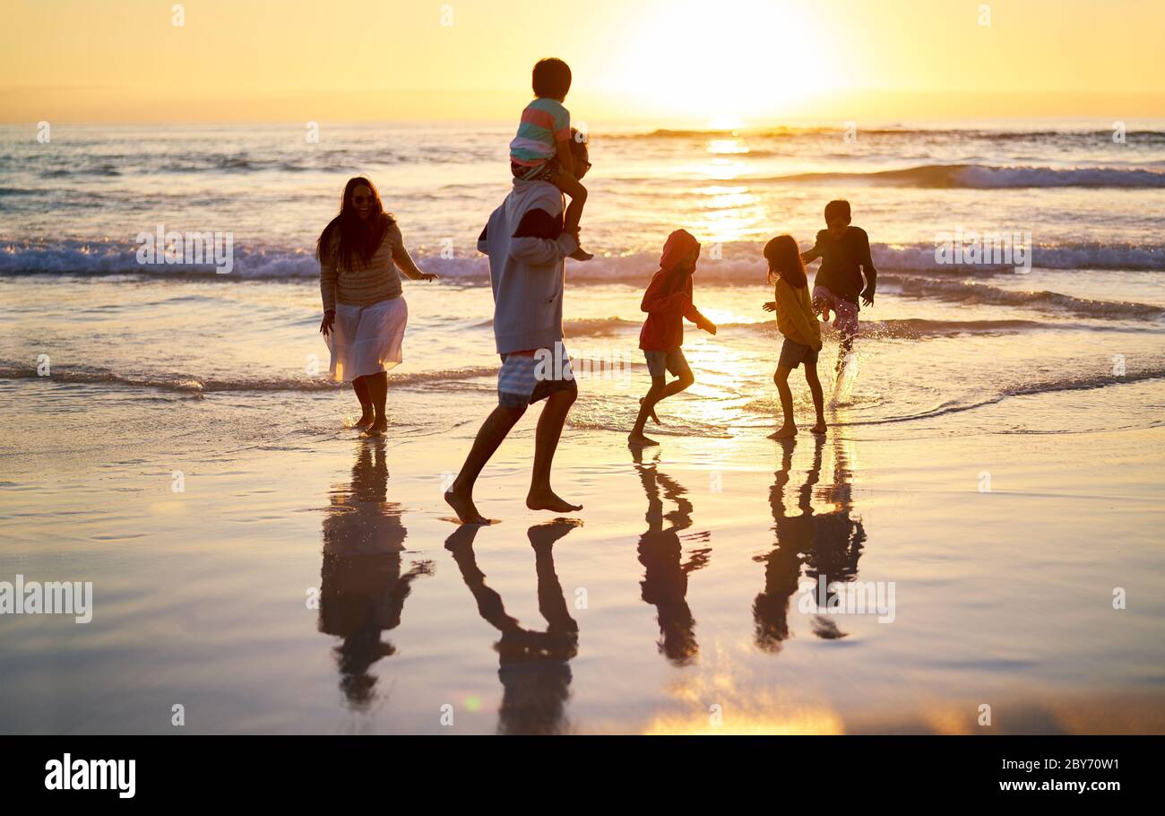 Familie waten in der Brandung auf idyllischem Meeresstrand bei Sonnenuntergang Stockfoto