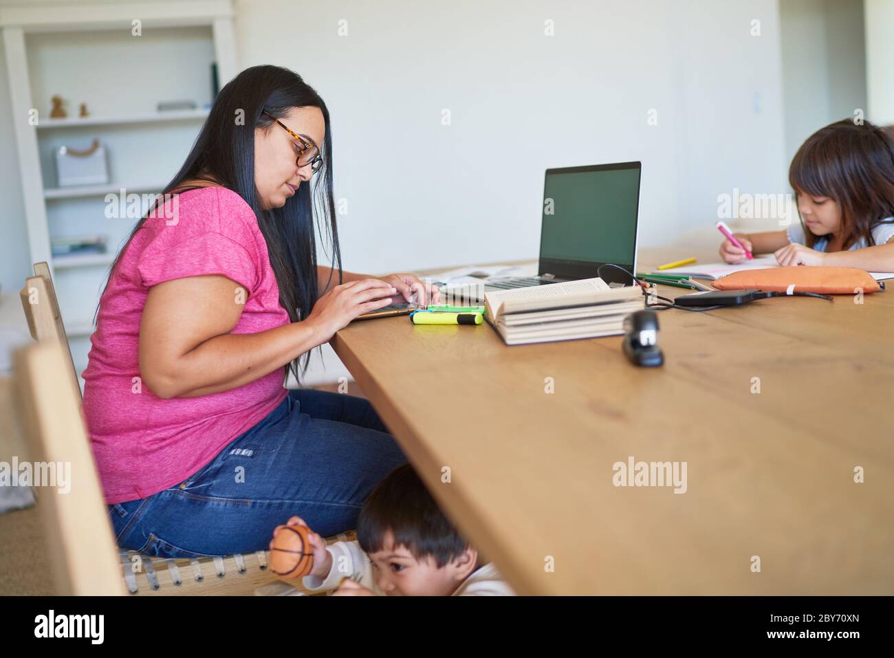 Kinder spielen und Hausaufgaben machen, während Mutter am Tisch arbeitet Stockfoto