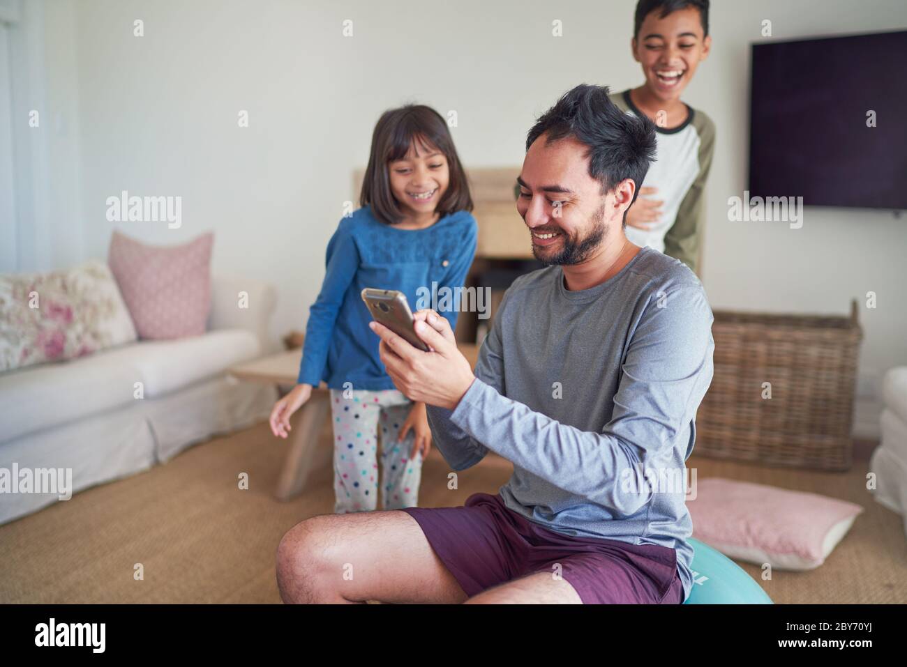 Glücklicher Vater und Kinder mit Smartphone im Wohnzimmer Stockfoto