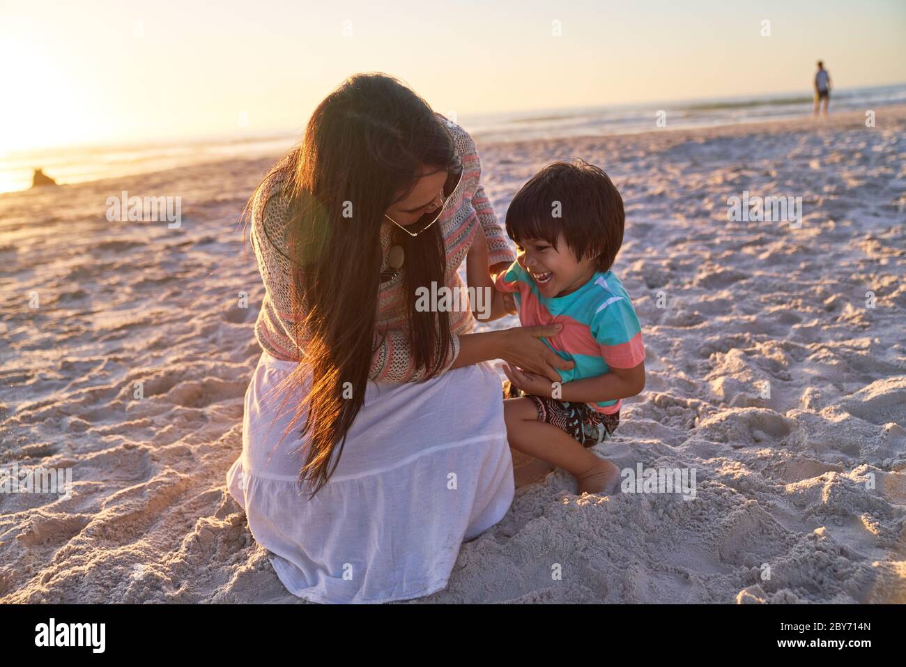 Verspielte Mutter kitzelt Sohn am Sonnenuntergang Strand Stockfoto