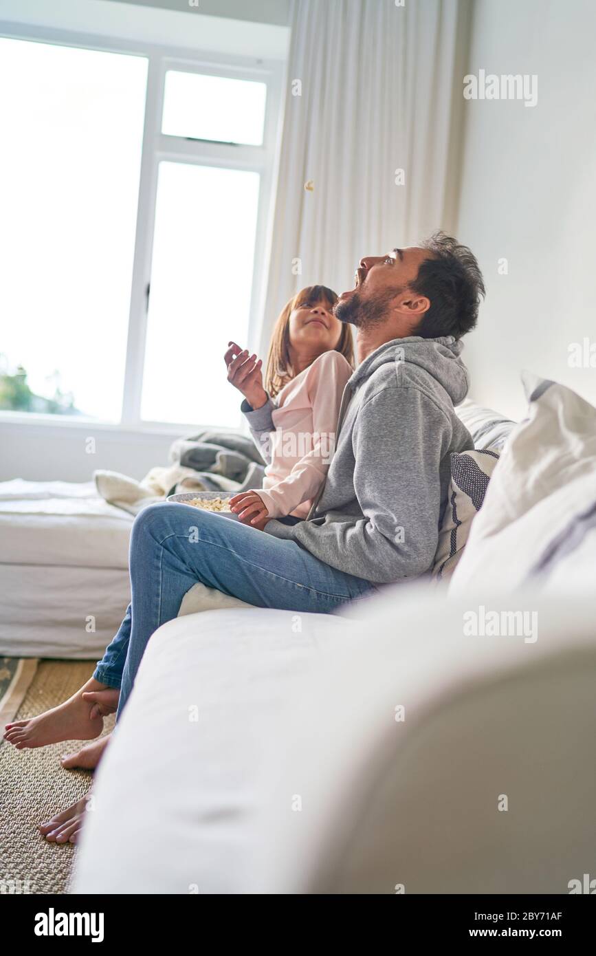 Verspielte Vater und Tochter essen Popcorn auf dem Sofa Stockfoto