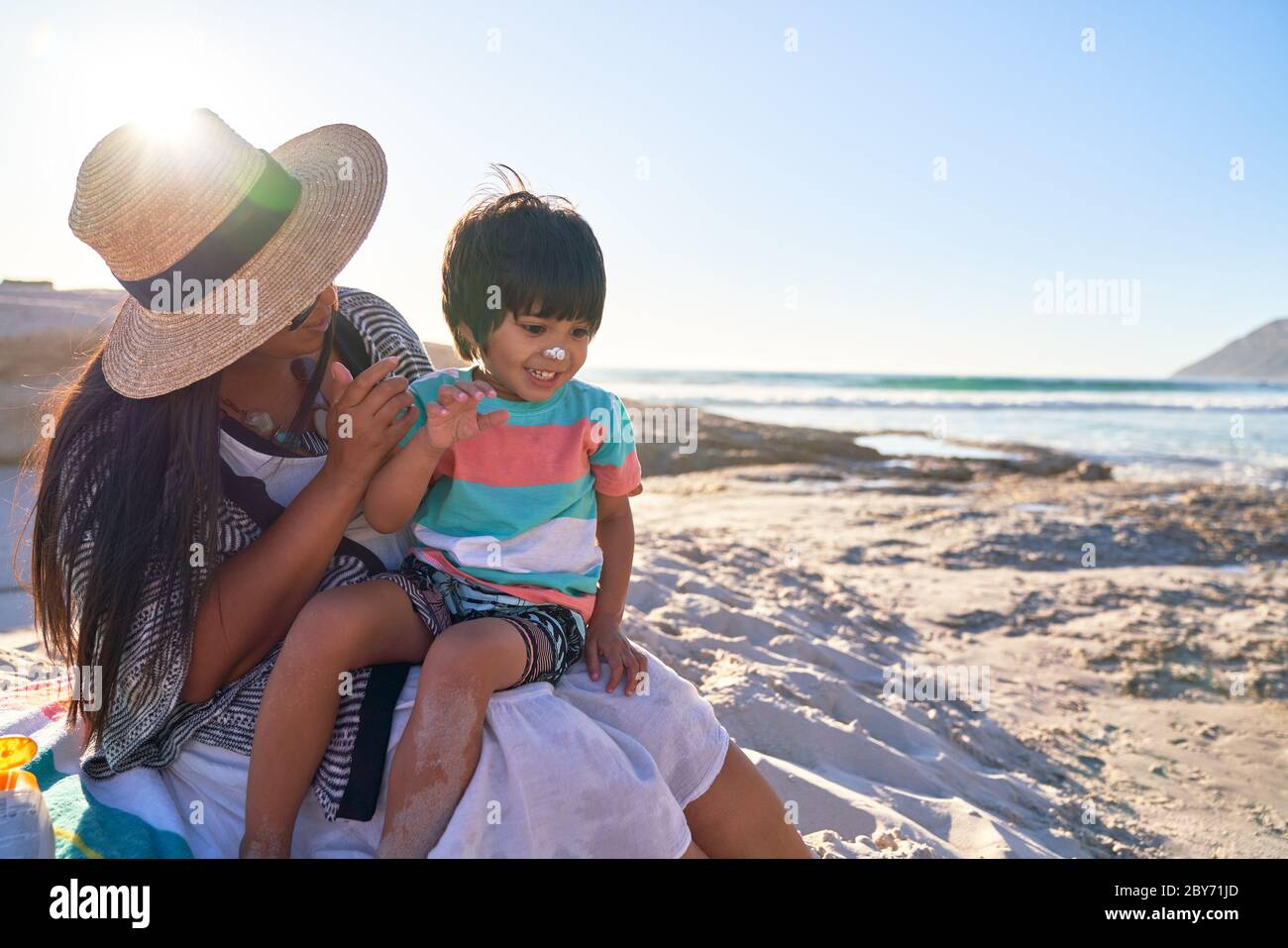 Mutter, die Sonnencreme auf die Nase des niedlichen Sohnes am sonnigen Strand anwendet Stockfoto