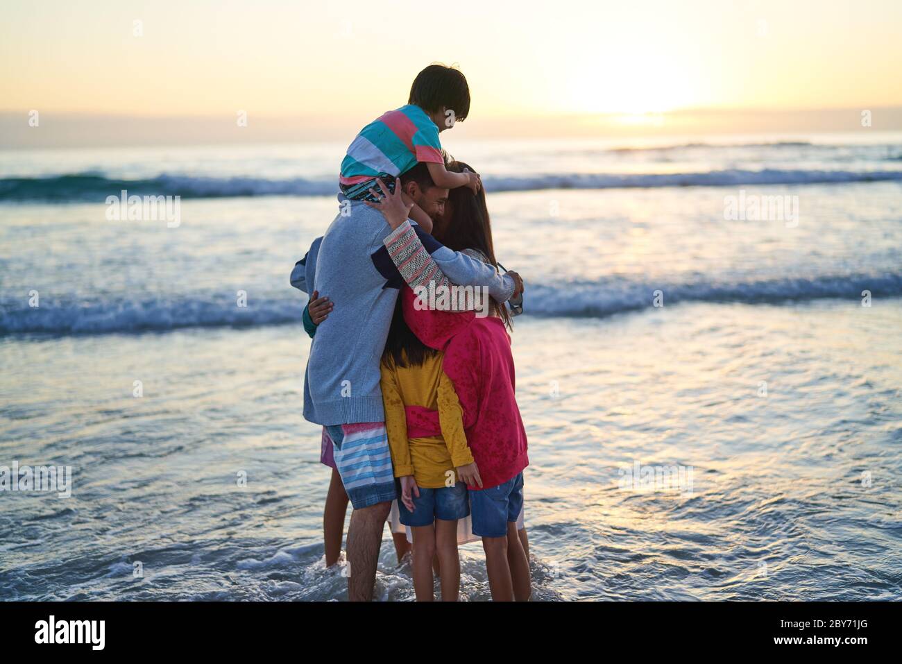Glückliche liebevolle Familie umarmt in Ozean surfen bei Sonnenuntergang Stockfoto