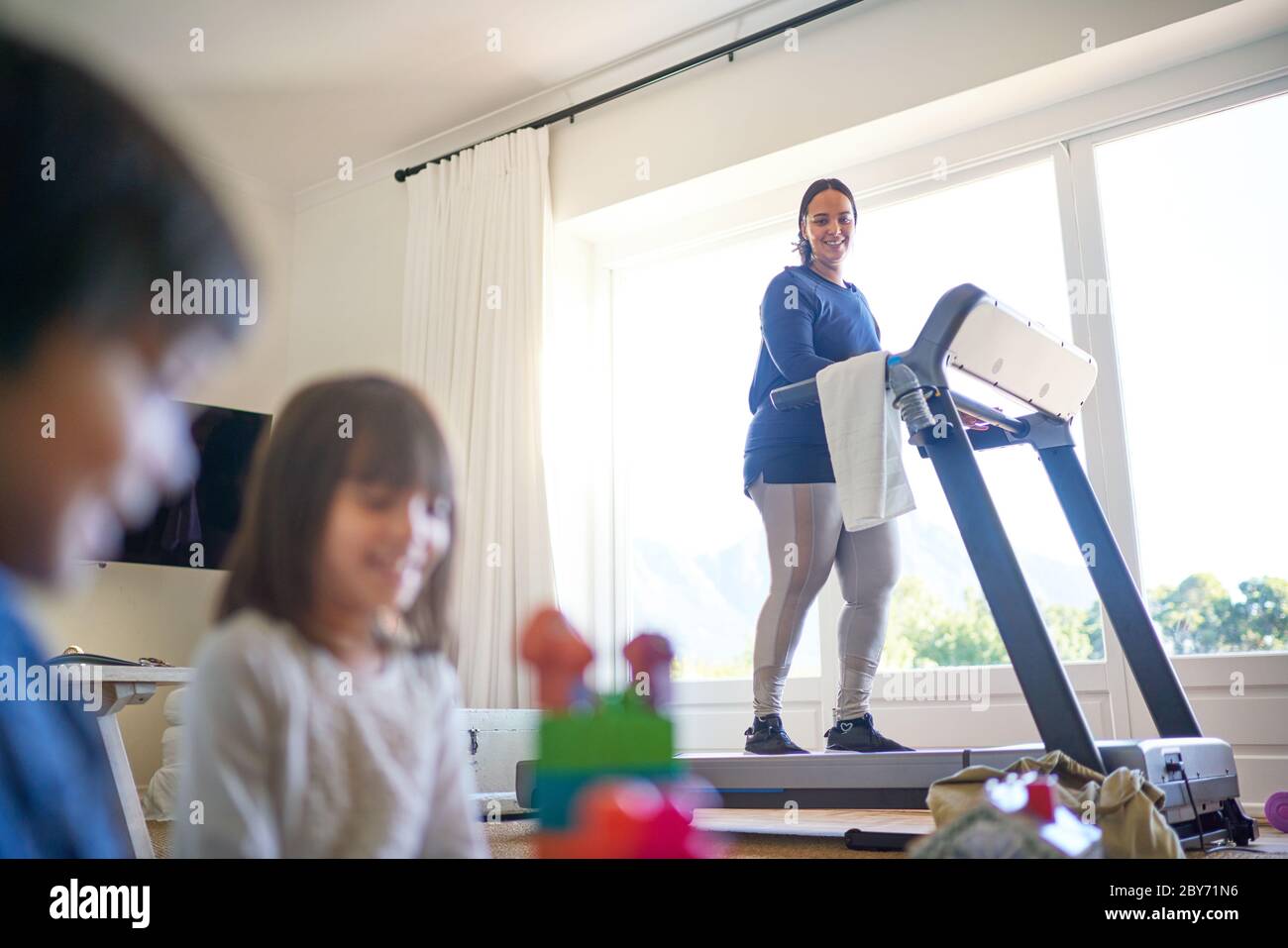 Mutter trainiert auf dem Laufband und beobachtet die Kinder beim Spielen Stockfoto