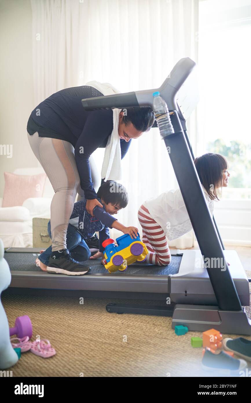 Kinder mit Spielzeug ablenkende Mutter auf Laufband Stockfoto