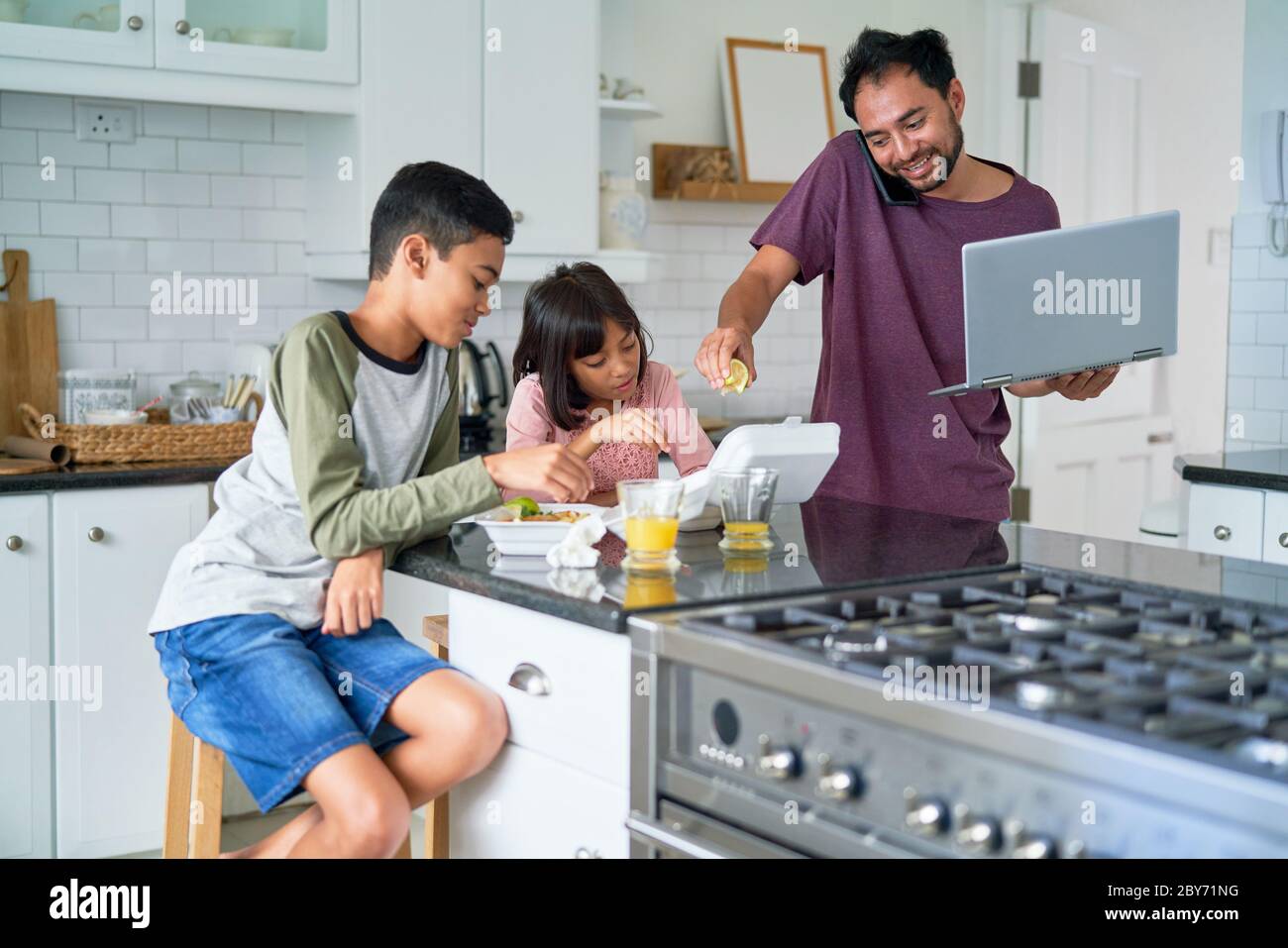 Vater mit Laptop füttert Kinder mit Essen zum Mitnehmen in der Küche Stockfoto