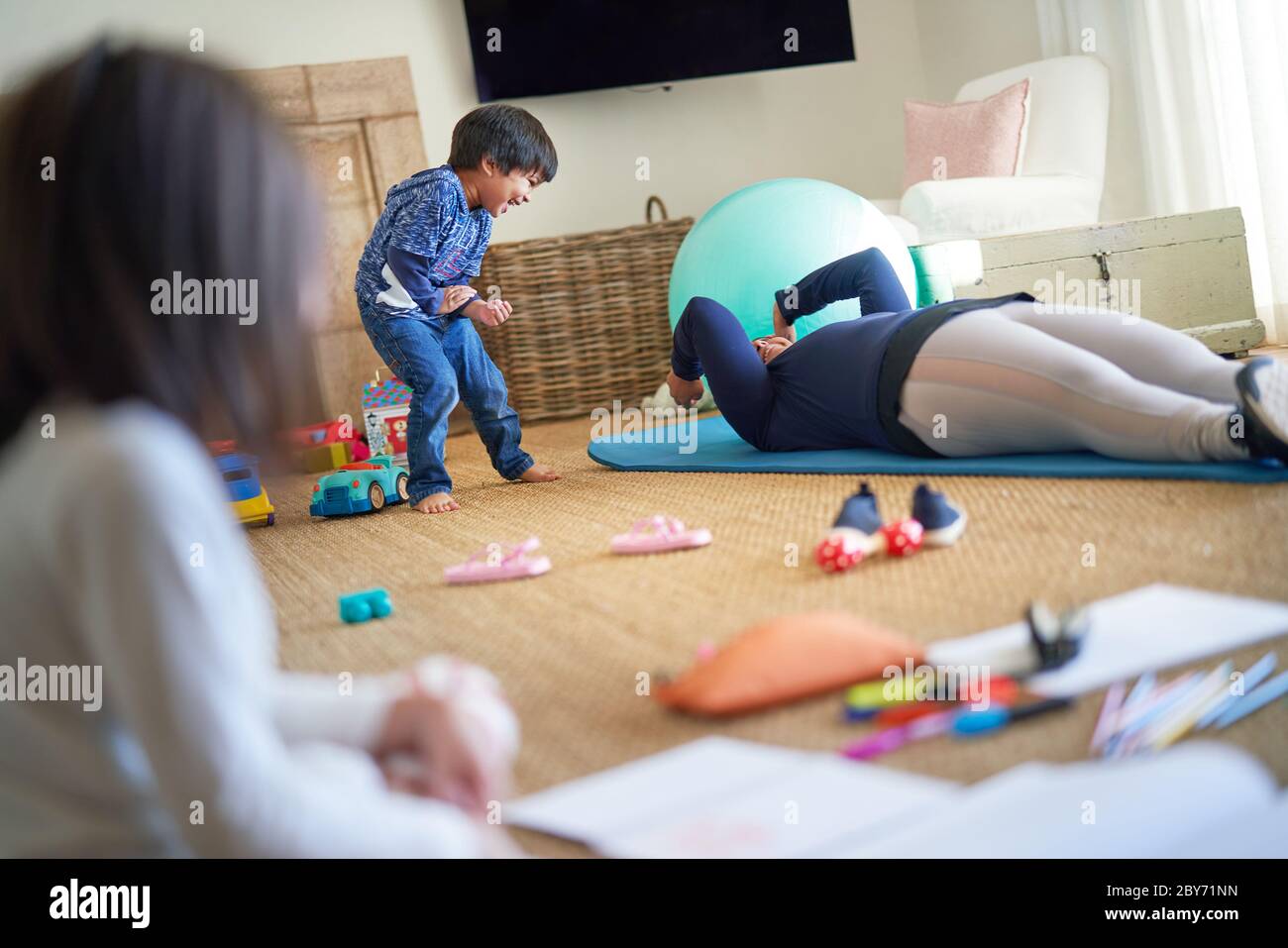 Verspielter Junge beobachten Mutter Übung auf Wohnzimmer Boden Stockfoto