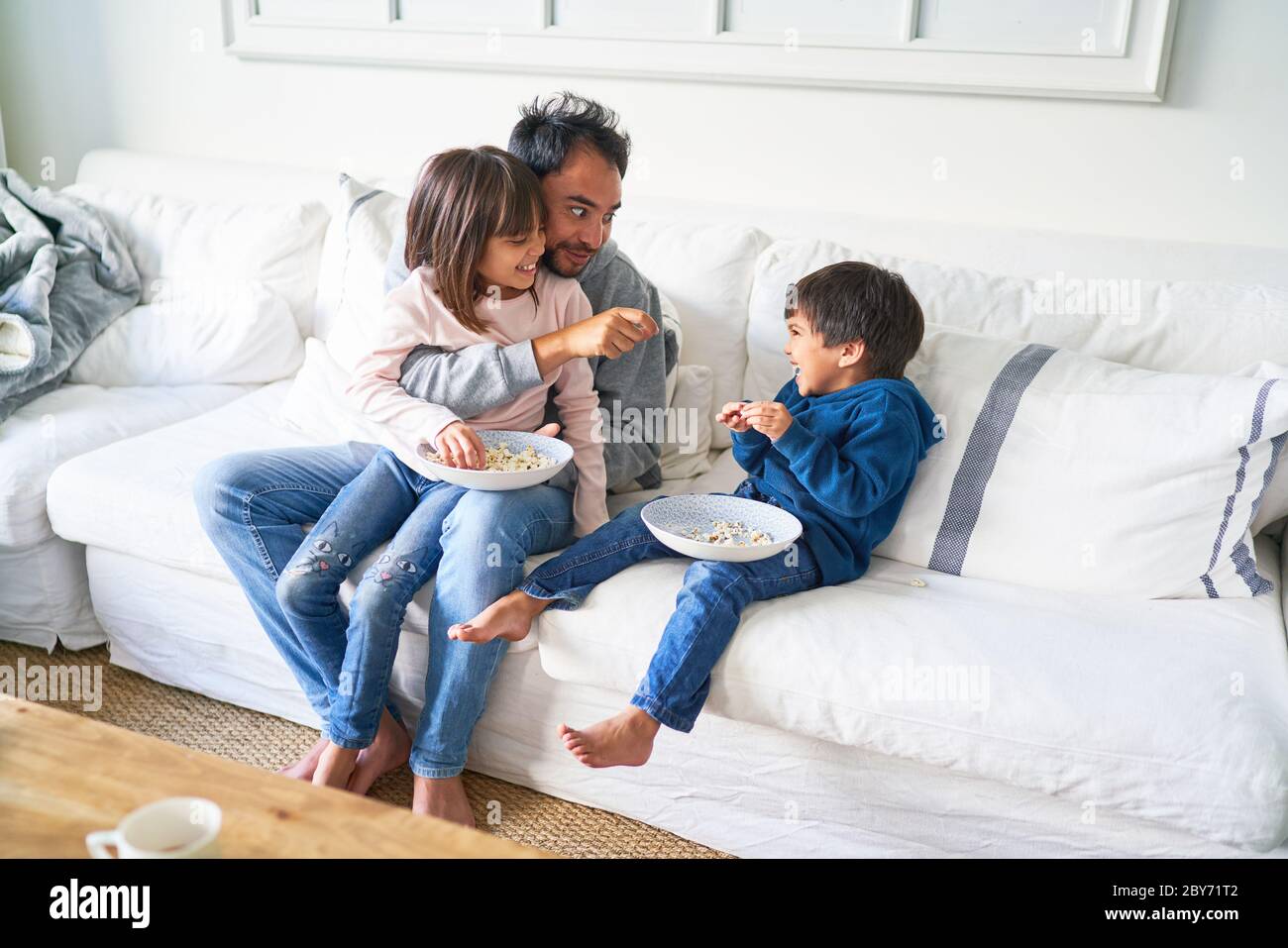 Vater und Kinder essen Popcorn auf dem Sofa im Wohnzimmer Stockfoto