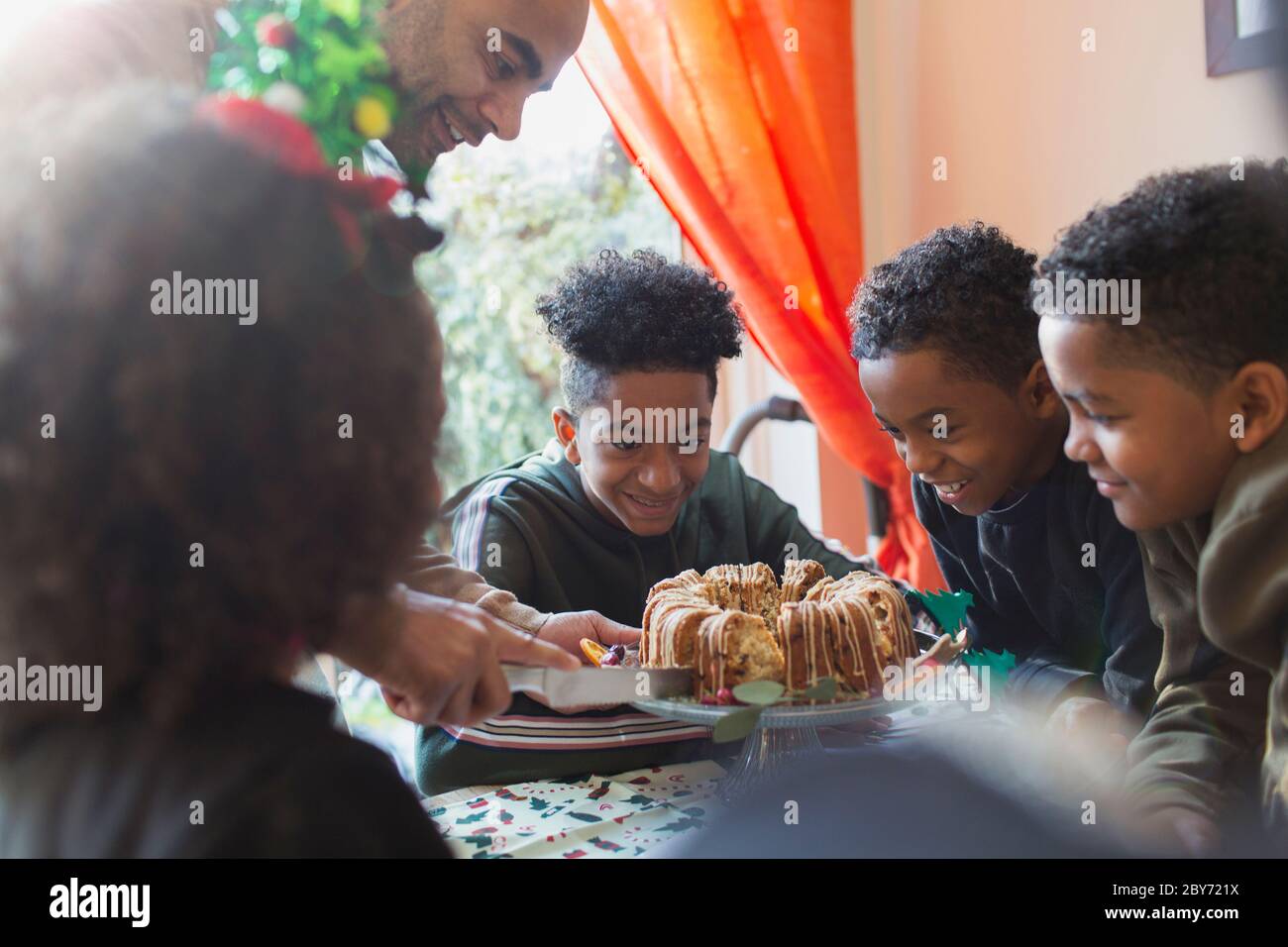 Vater serviert Weihnachtskuchen, um eifrige Söhne am Tisch Stockfoto