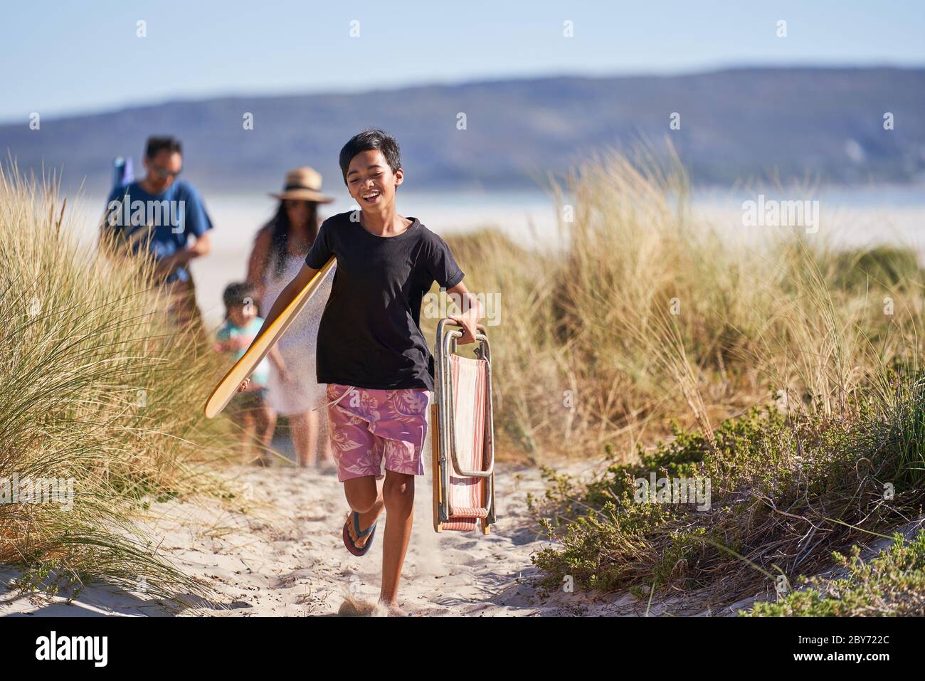 Happy Boy läuft mit Klappstuhl auf sonnigen Strand Weg Stockfoto