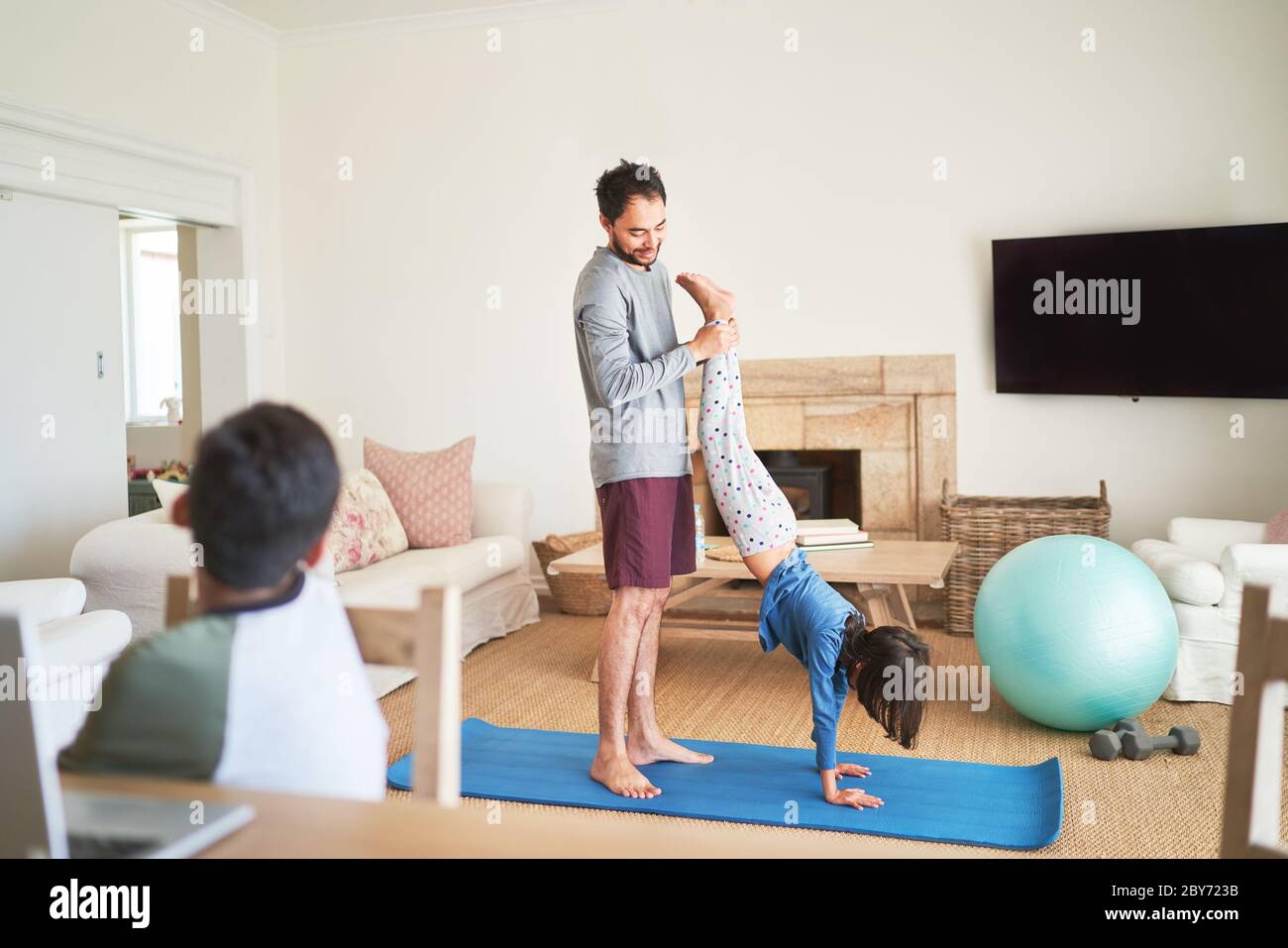 Vater hilft Tochter auf Yoga-Matte im Wohnzimmer Handstand Stockfoto