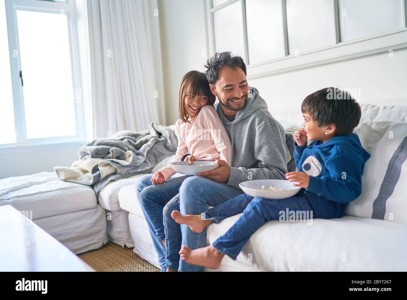 Glücklicher Vater und Kinder essen Popcorn auf Wohnzimmer Sofa Stockfoto