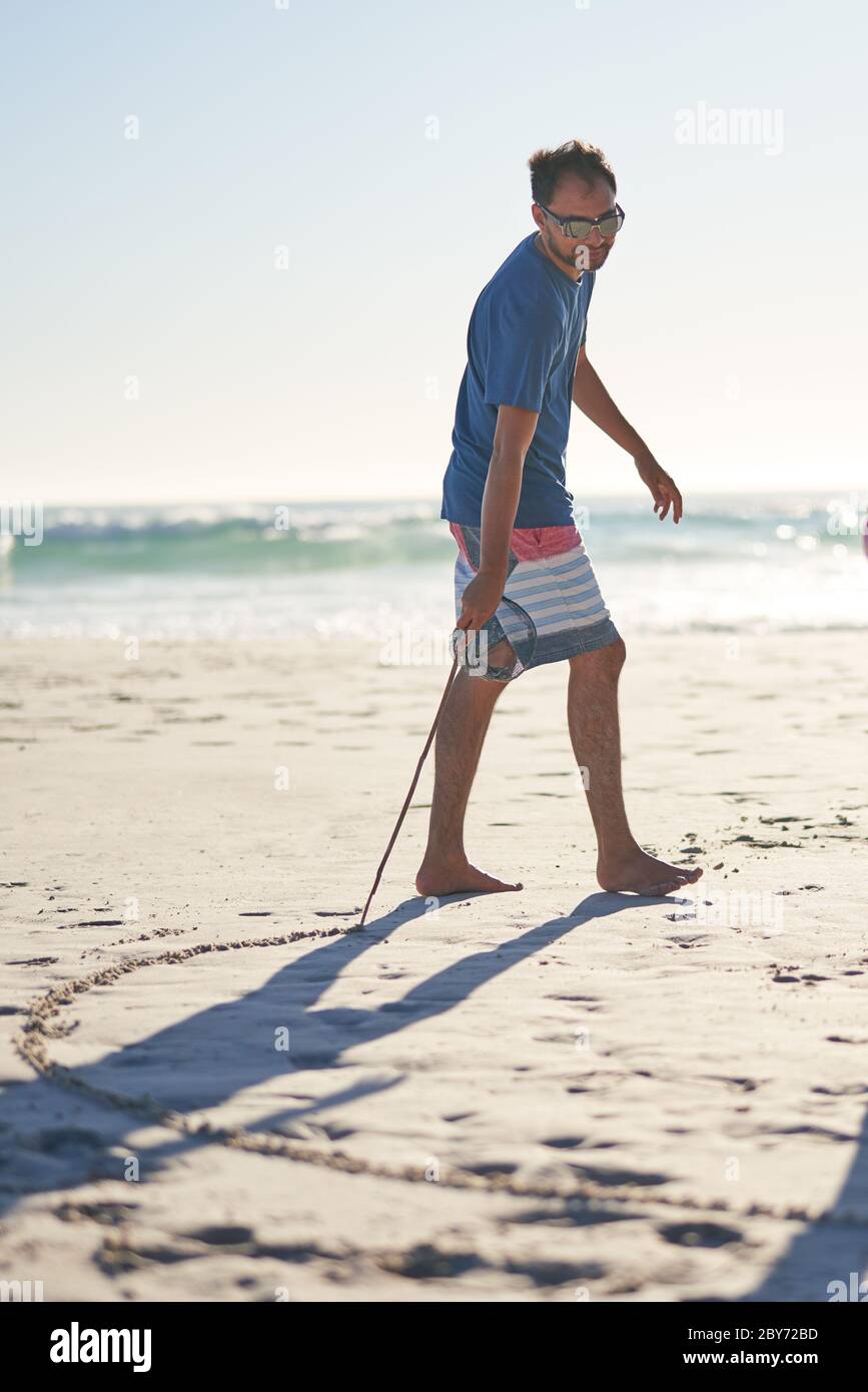 Mann, der mit Stock im Sand am sonnigen Strand zeichnet Stockfoto