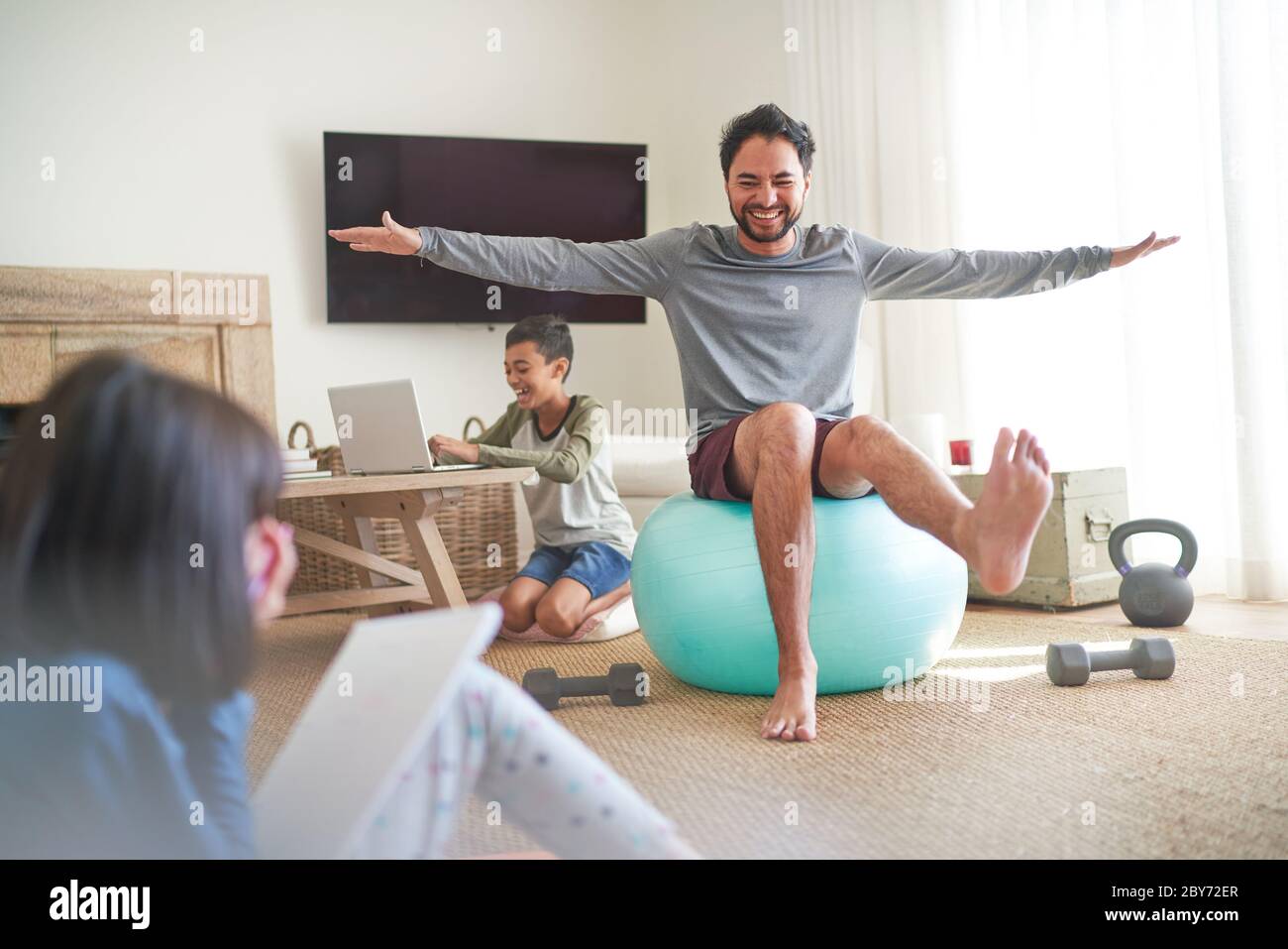 Spielerischer Vater beim Training auf Fitnessball im Wohnzimmer mit Kindern Stockfoto