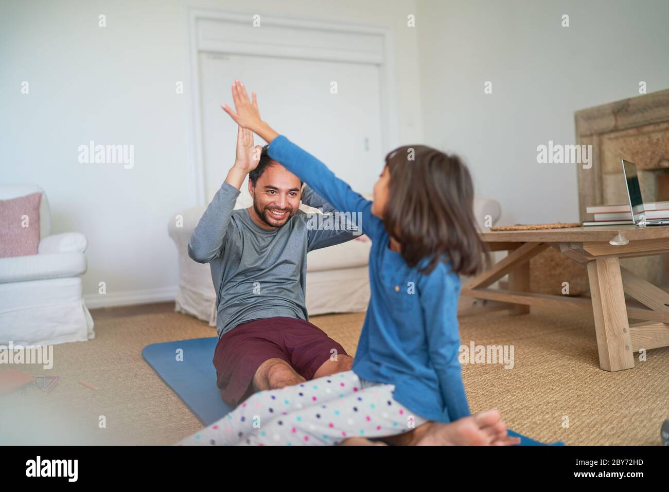 Glücklicher Vater und Tochter, die im Wohnzimmer auf einer Yogamatte fiving Stockfoto