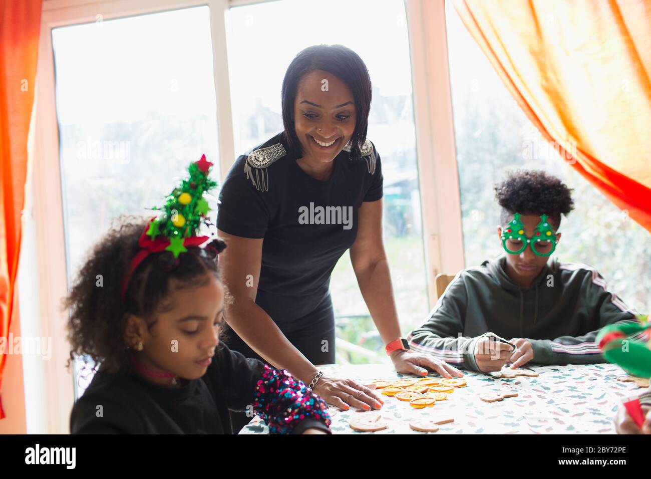 Glückliche Mutter und Kinder dekorieren Weihnachtskekse am Tisch Stockfoto