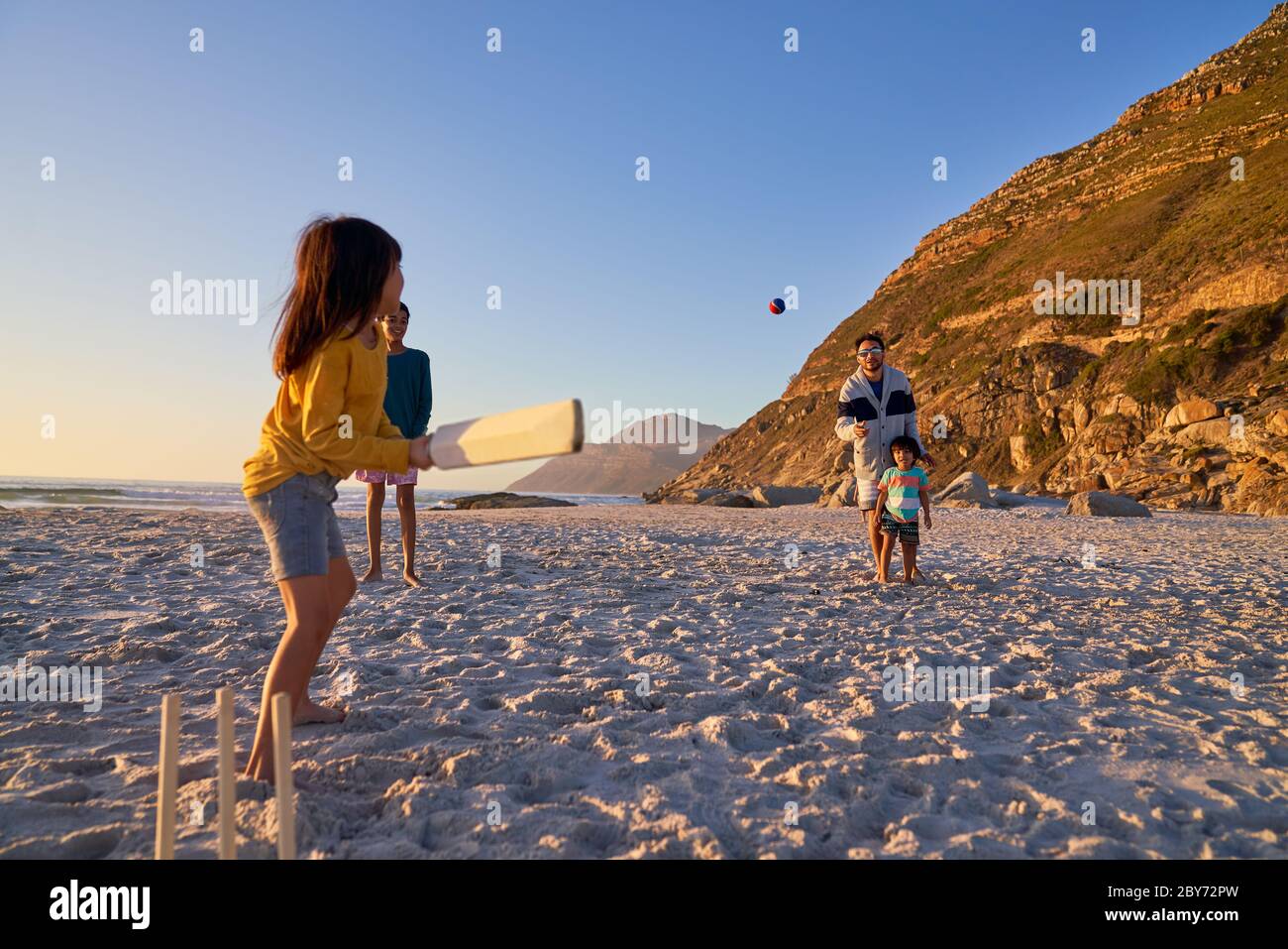 Familie spielt Cricket am sonnigen Strand Stockfoto