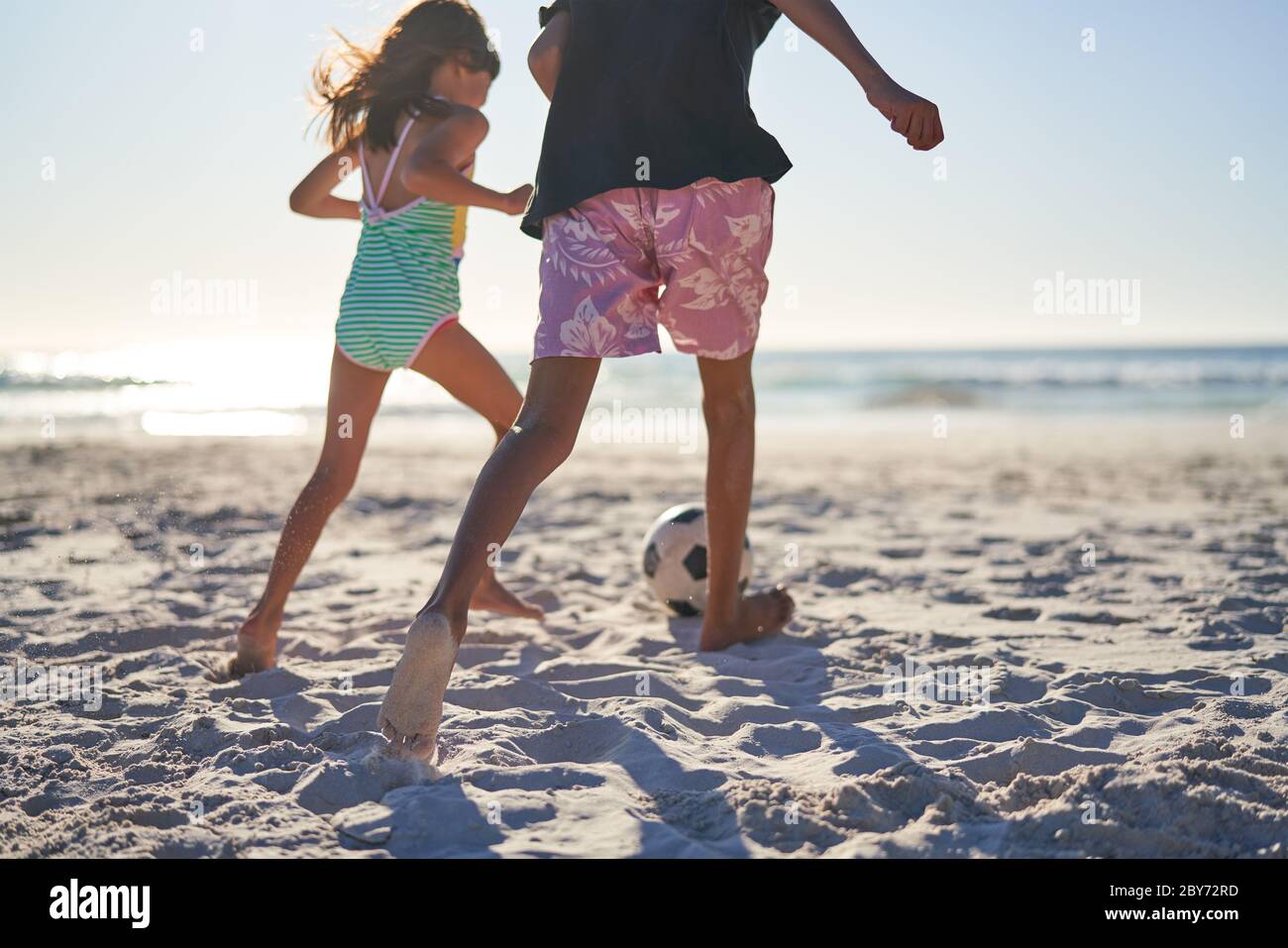 Bruder und Schwester spielen Fußball am sonnigen Strand Stockfoto