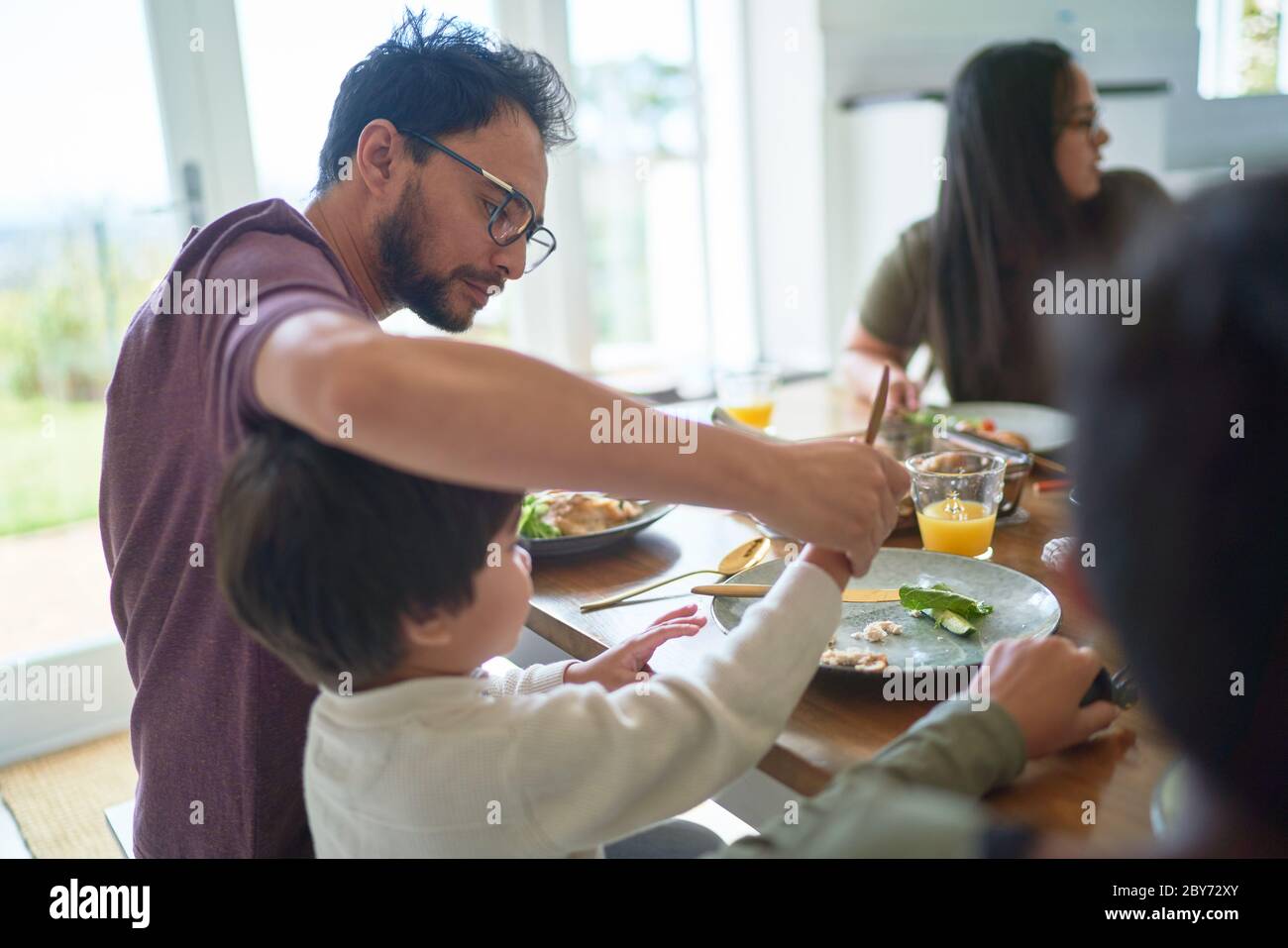 Vater hilft Sohn schneiden Essen am Esstisch Stockfoto