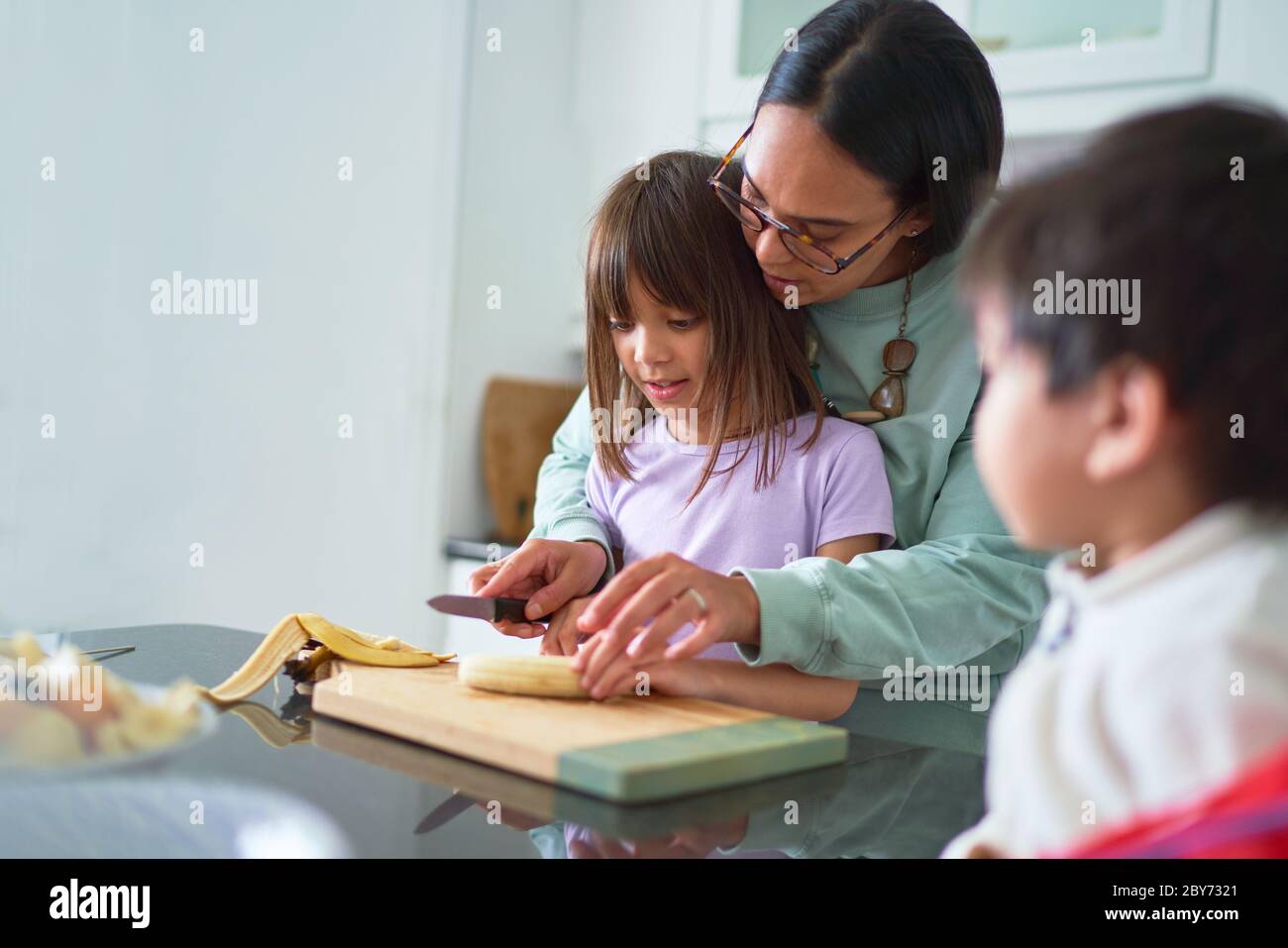 Mutter hilft Tochter schneiden Banane in der Küche Stockfoto