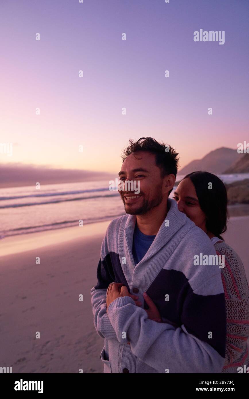 Liebevolles Paar umarmt am Meeresstrand bei Sonnenuntergang Stockfoto