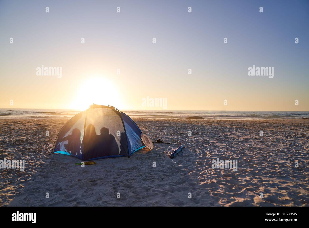 Silhouette der Familie im Zelt am sonnigen Strand bei Sonnenuntergang Stockfoto